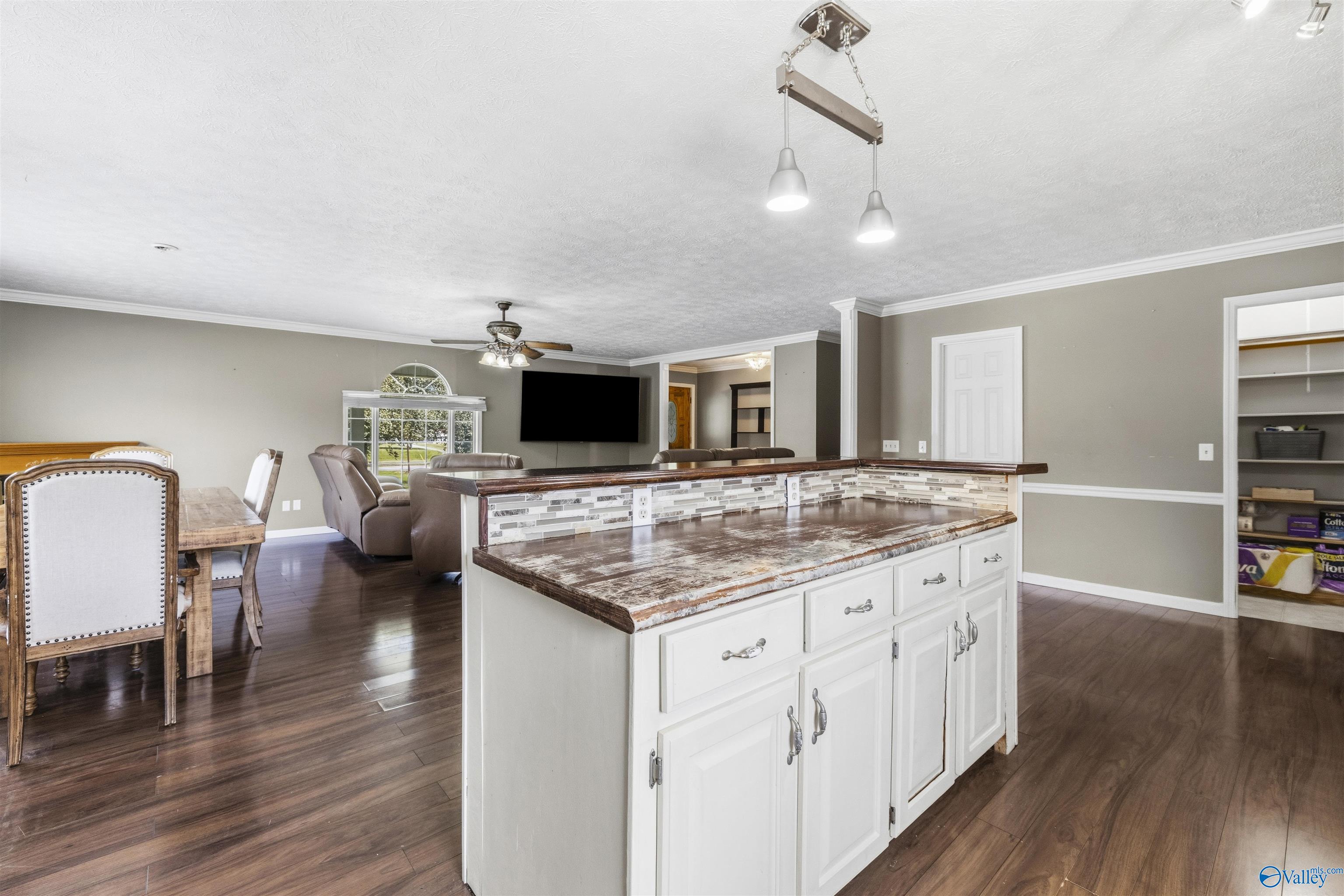 Open-plan kitchen with a large white island and dark wood countertop, overlooking dining and living areas.