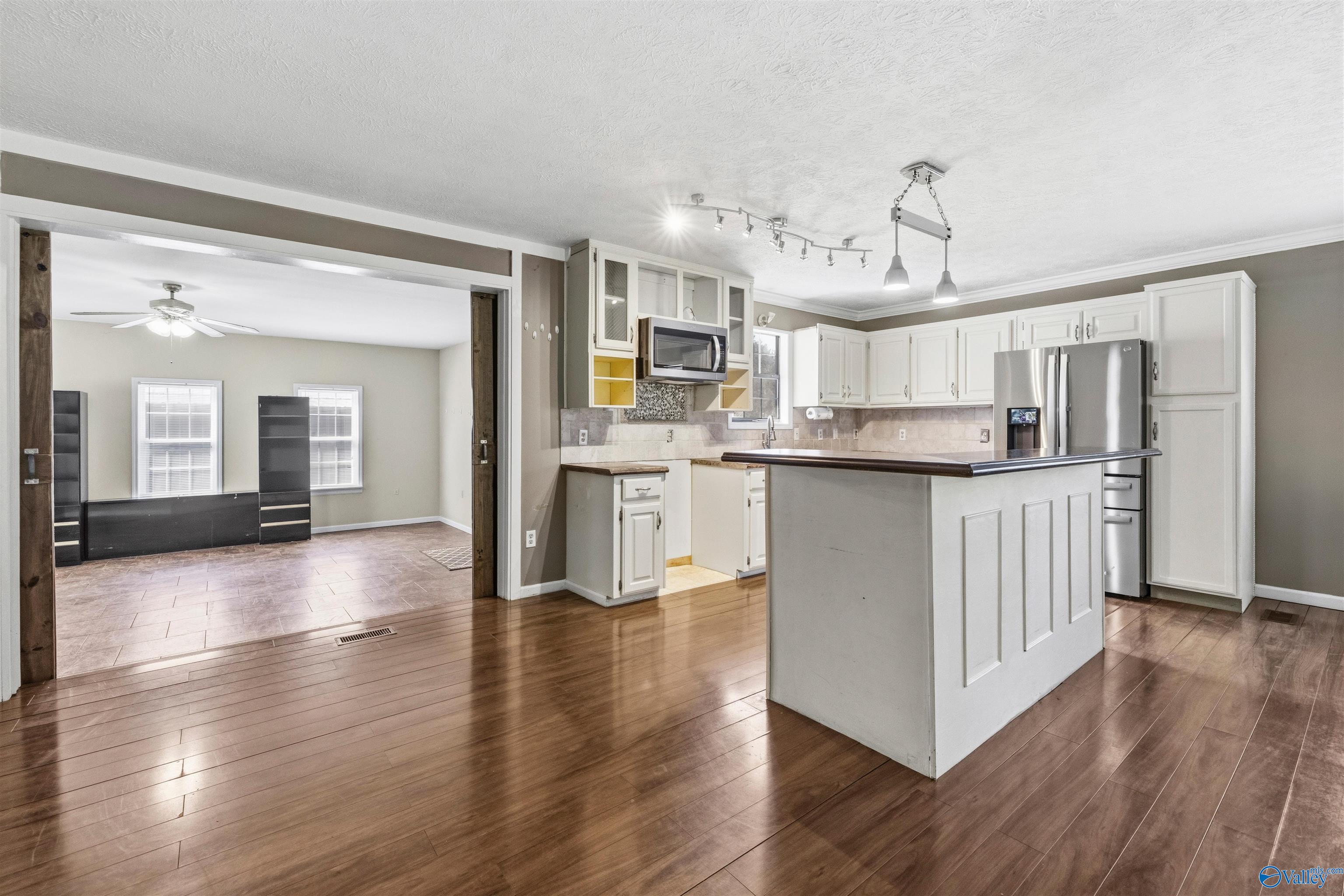 Kitchen with a large white island, stainless steel appliances, and wood floors adjoining a tiled room.
