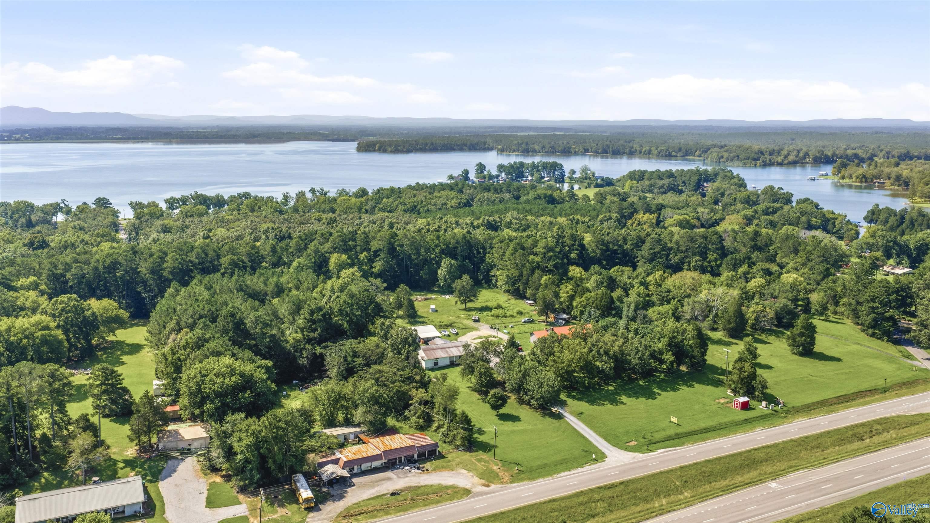 Aerial view of wooded acreage beside Weiss Lake, with buildings, open lawns, and highway frontage.