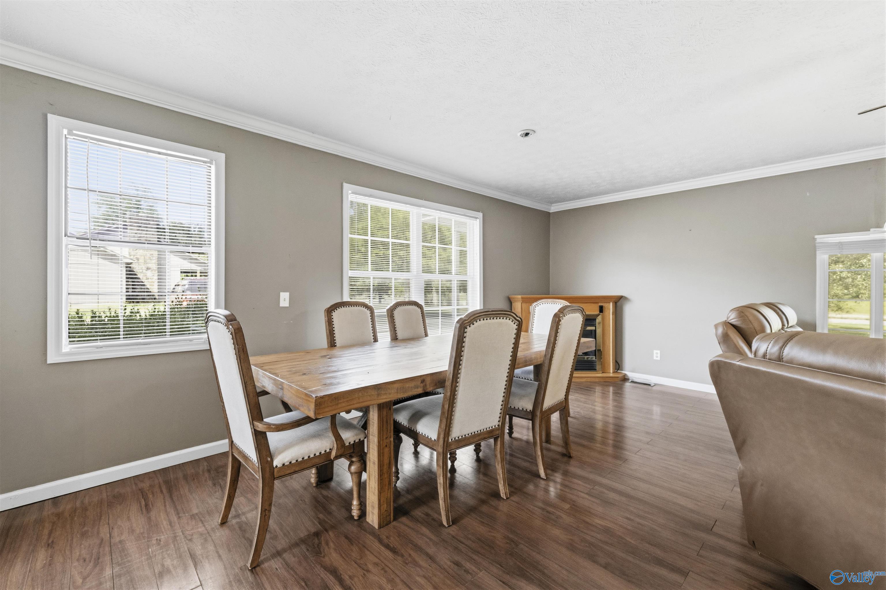 Dining area with a wooden table and upholstered chairs beside a living room with a leather sofa.