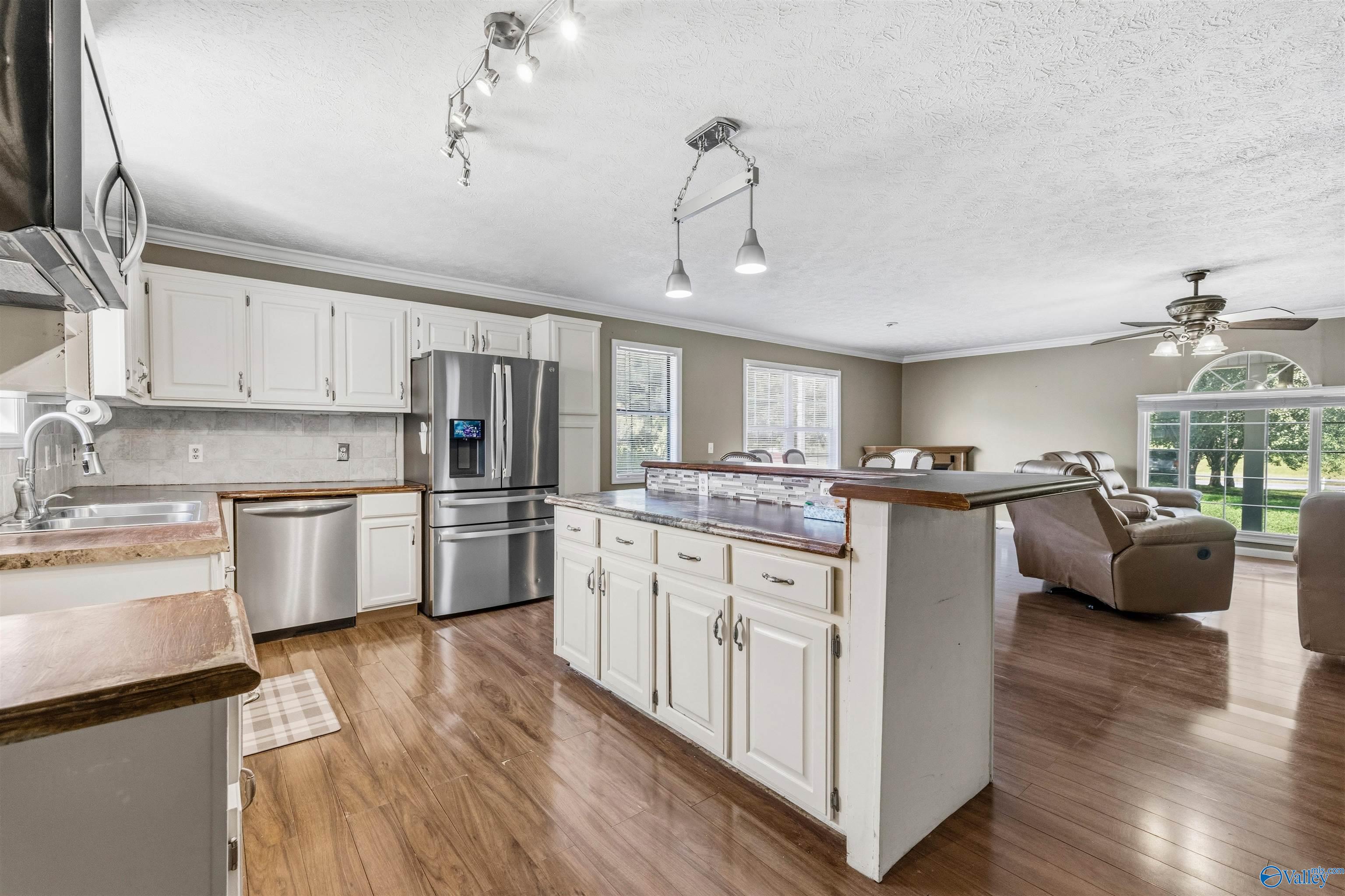 Kitchen with white cabinets and stainless appliances, opening to a living area with leather recliners.