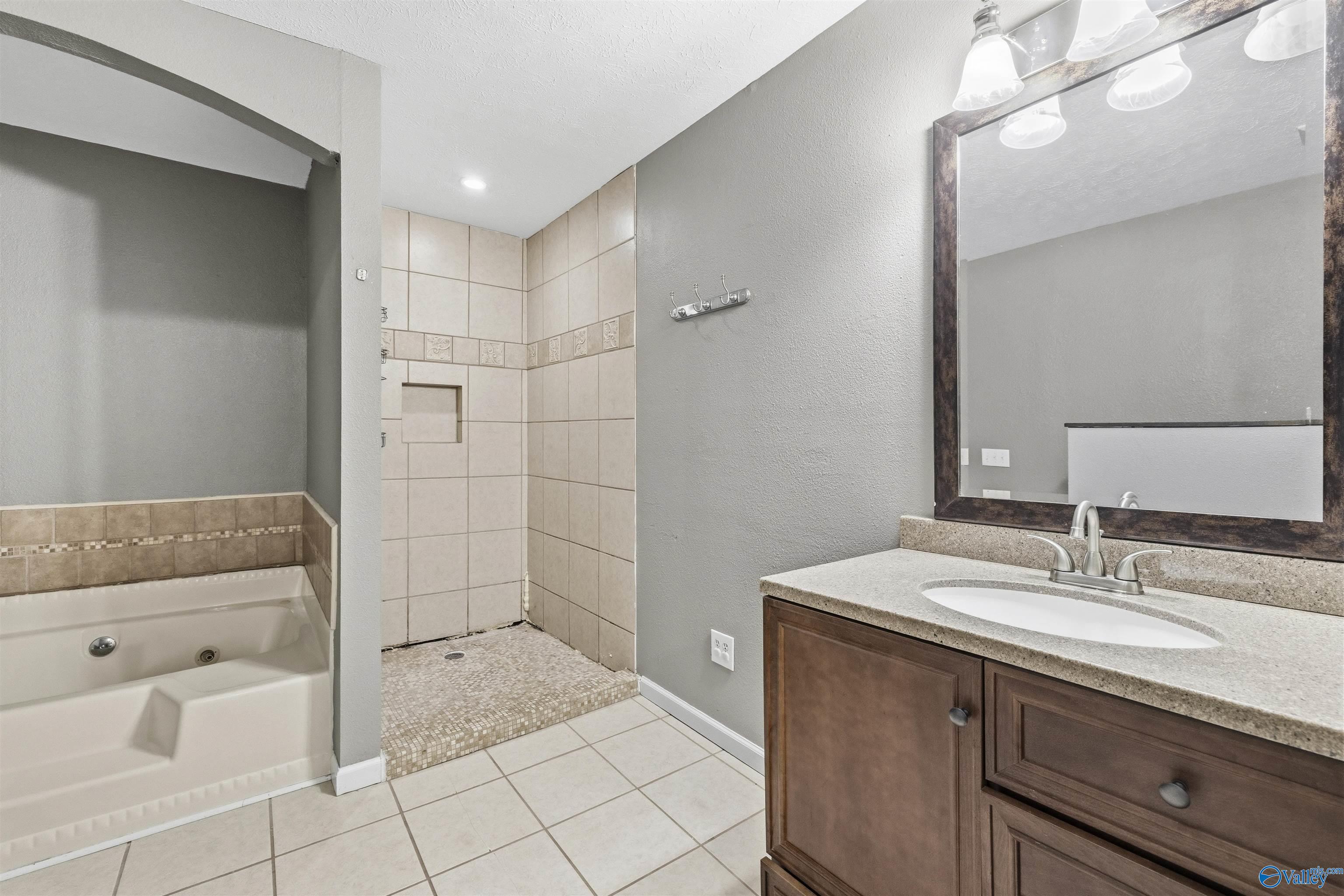 Bathroom with tiled walk-in shower, jetted tub, and wood vanity.