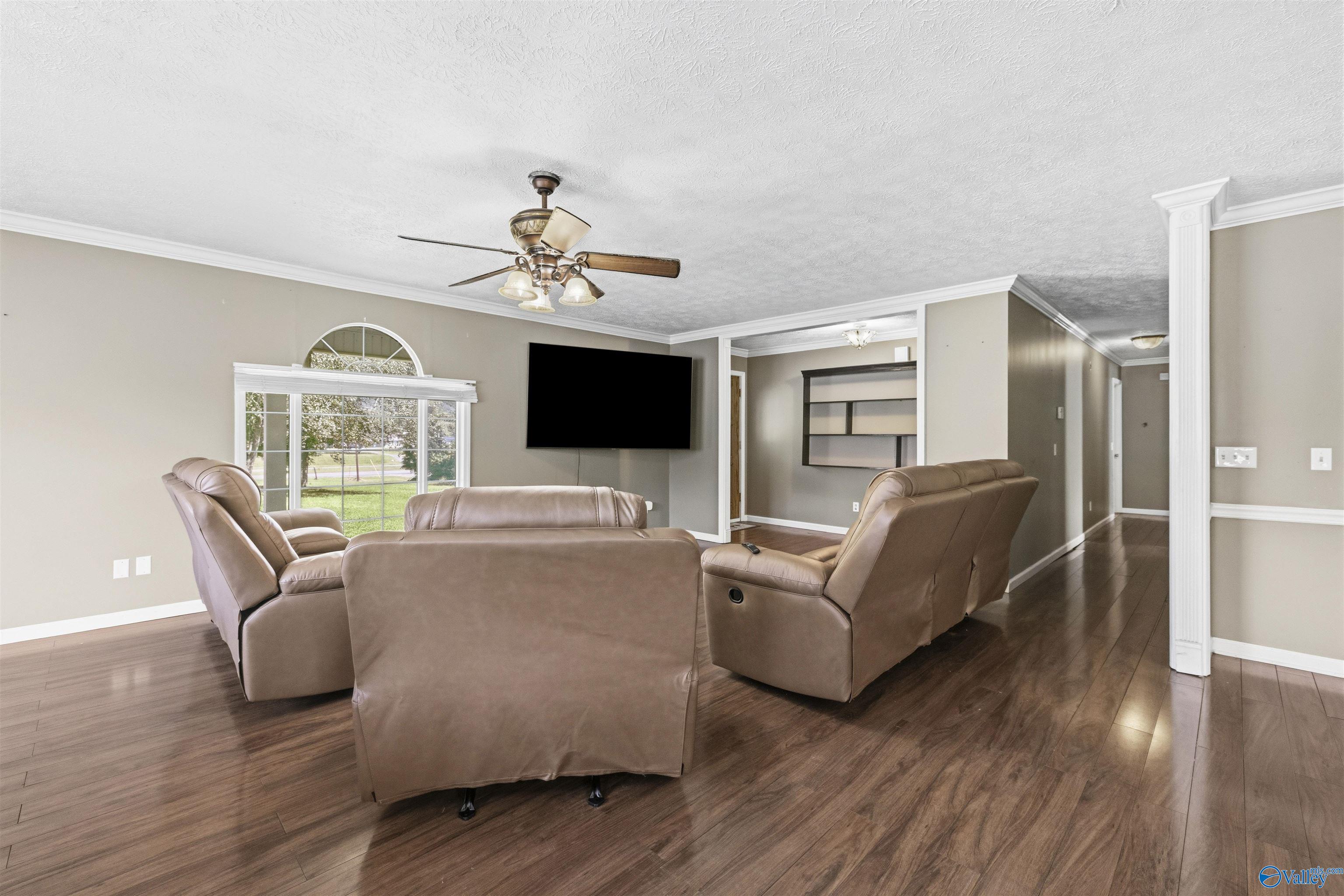 Living room with brown leather recliners, dark wood floors, and a large window overlooking a green yard.
