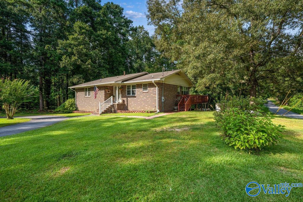 Single-story brick house with a broad green lawn, mature trees, and a wooden deck.