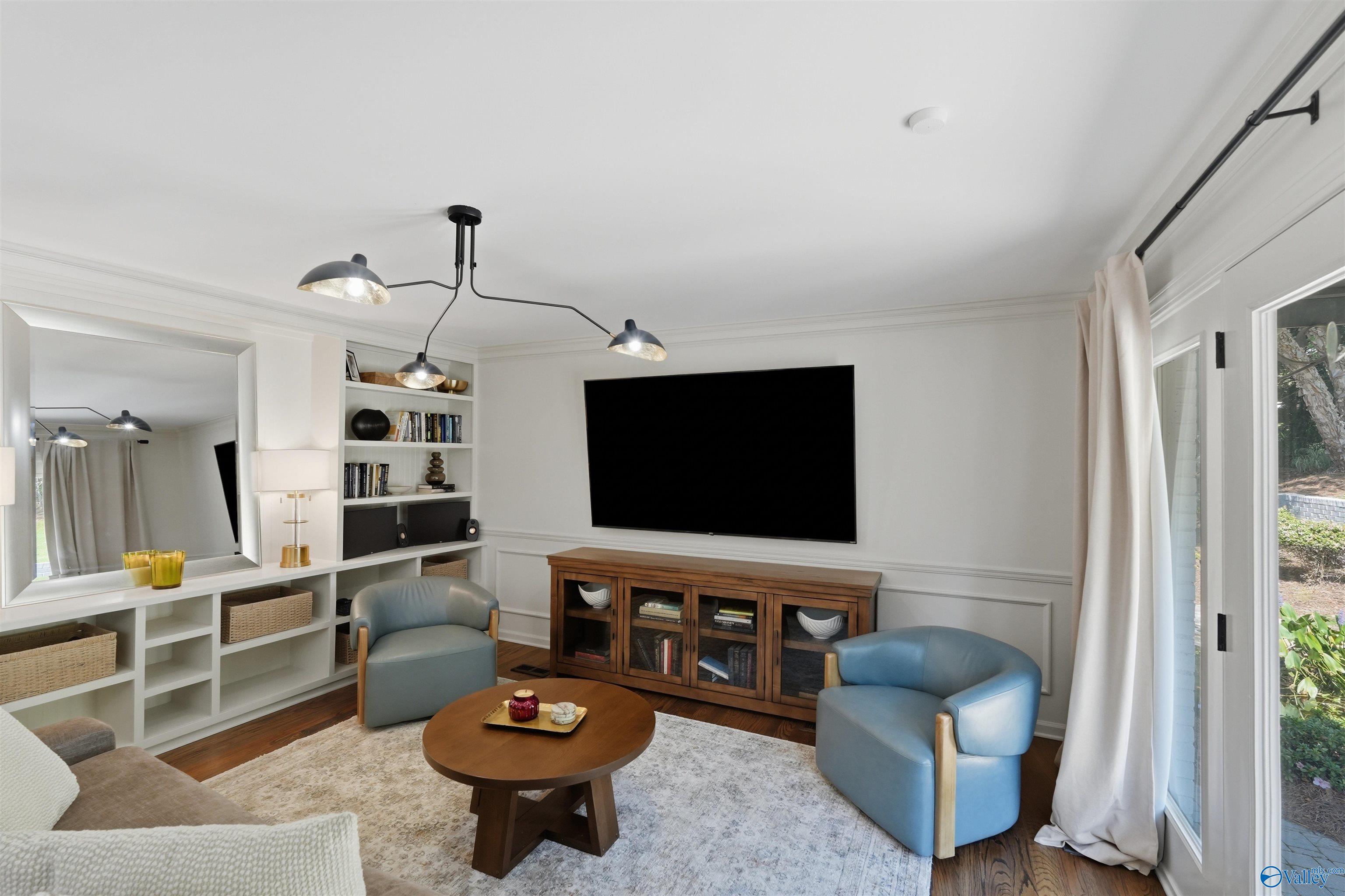 Living room with built-in shelving, a large television, blue armchairs, and glass doors.