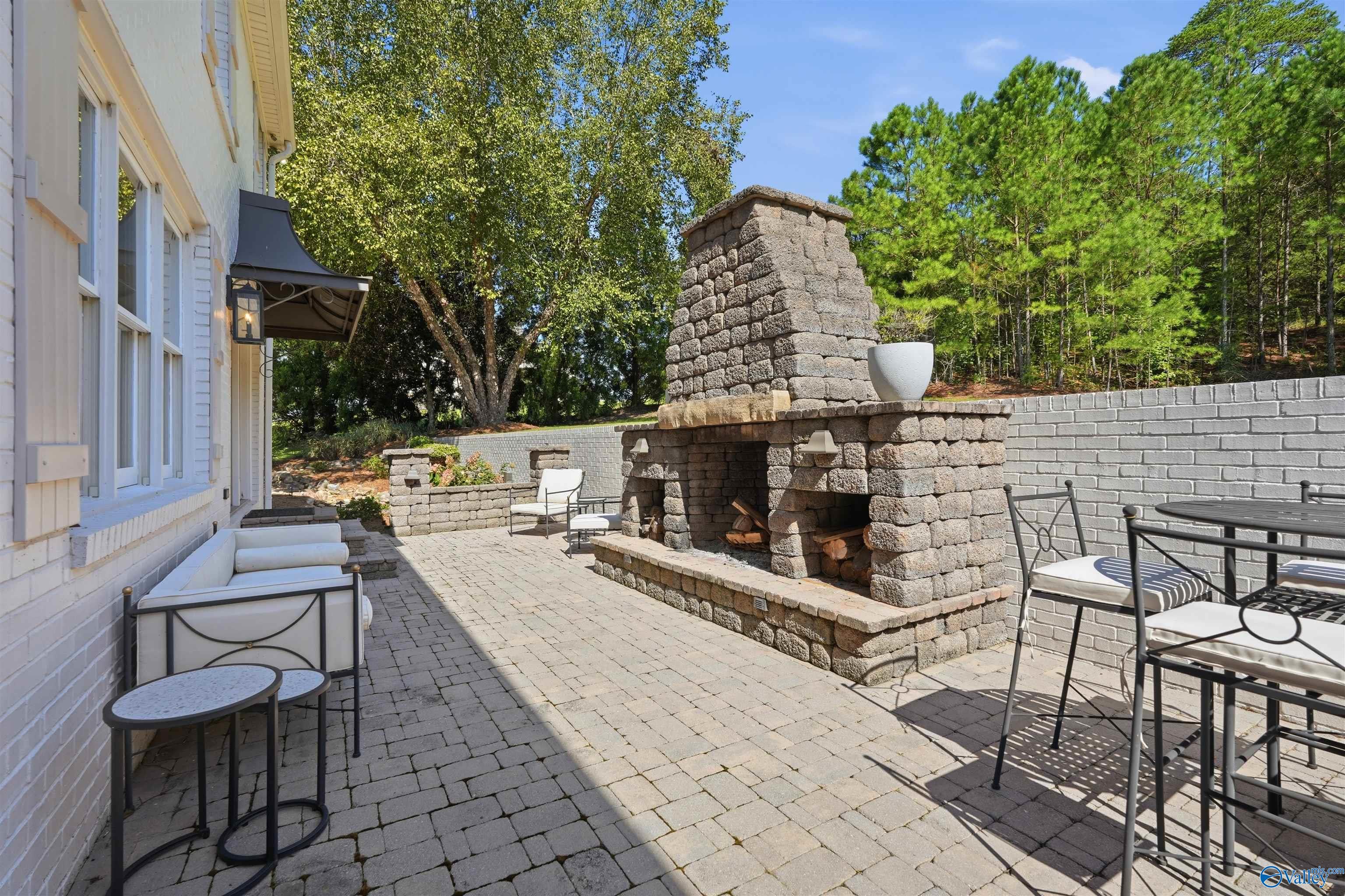 Stone patio with a large outdoor fireplace, white seating, and a dining table.