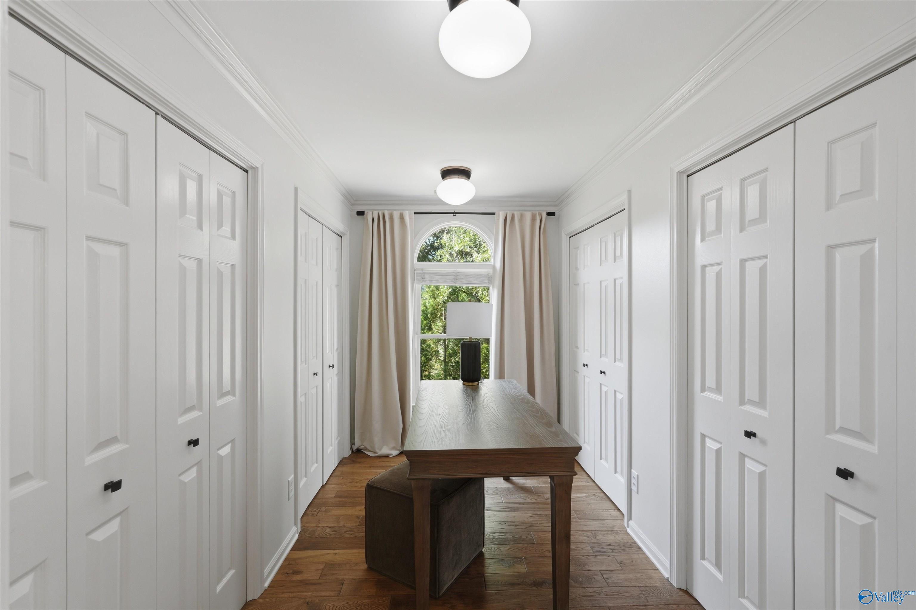 Hall lined with white paneled closet doors, a dark wood table, bench, and arched window.