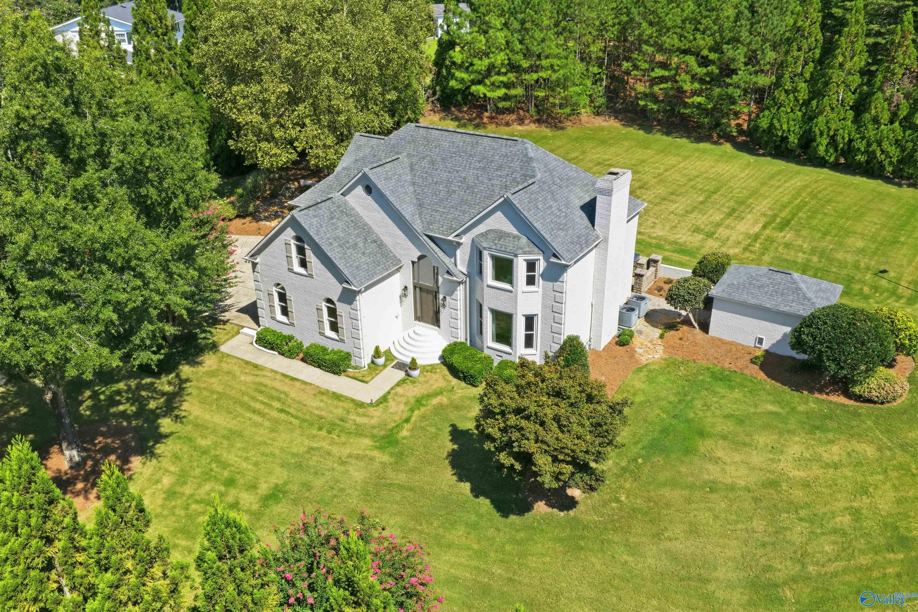 Aerial view of a gray brick house with a detached garage, broad lawn, and mature trees.