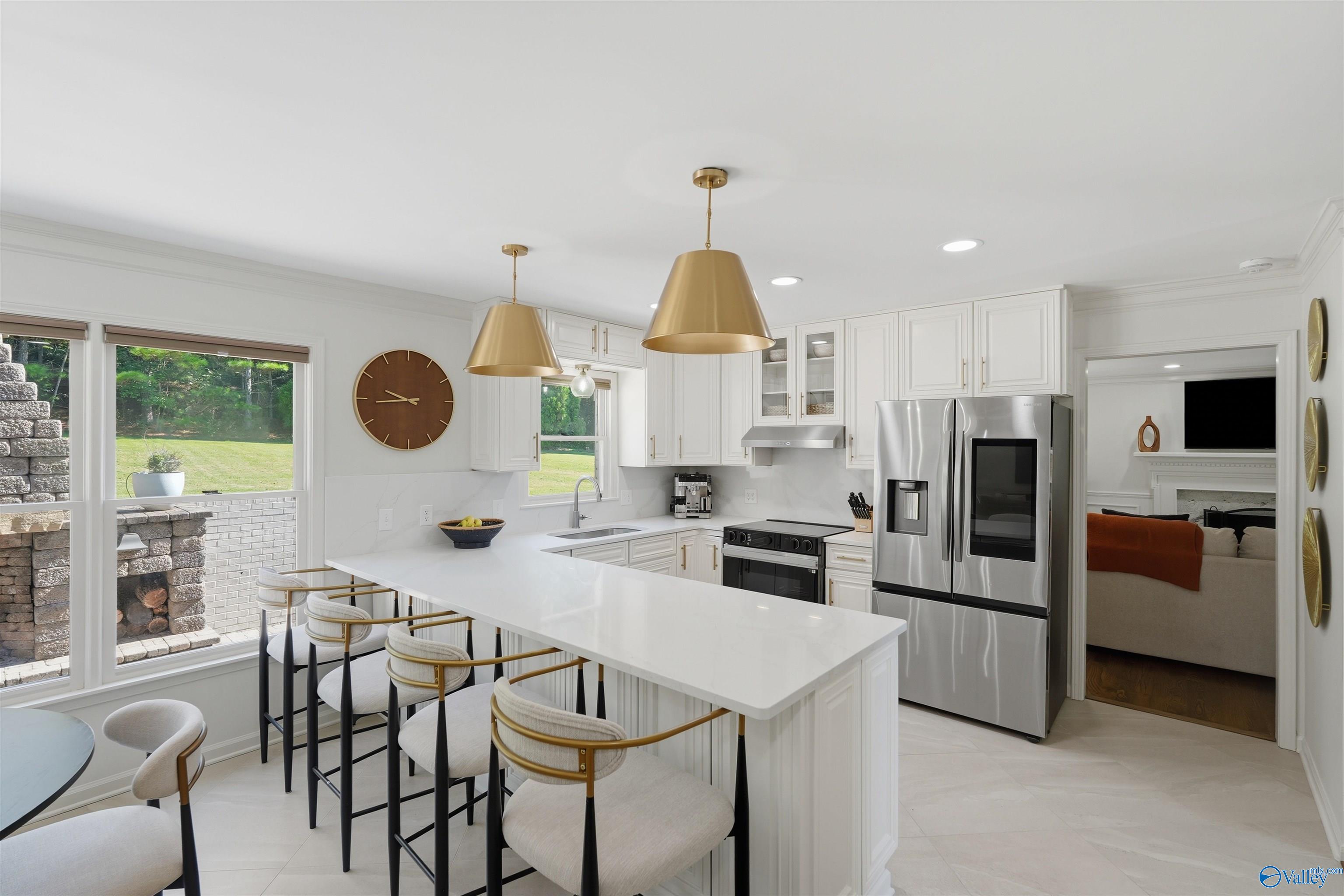 Bright white kitchen with a waterfall island, gold pendants, and stainless steel appliances.
