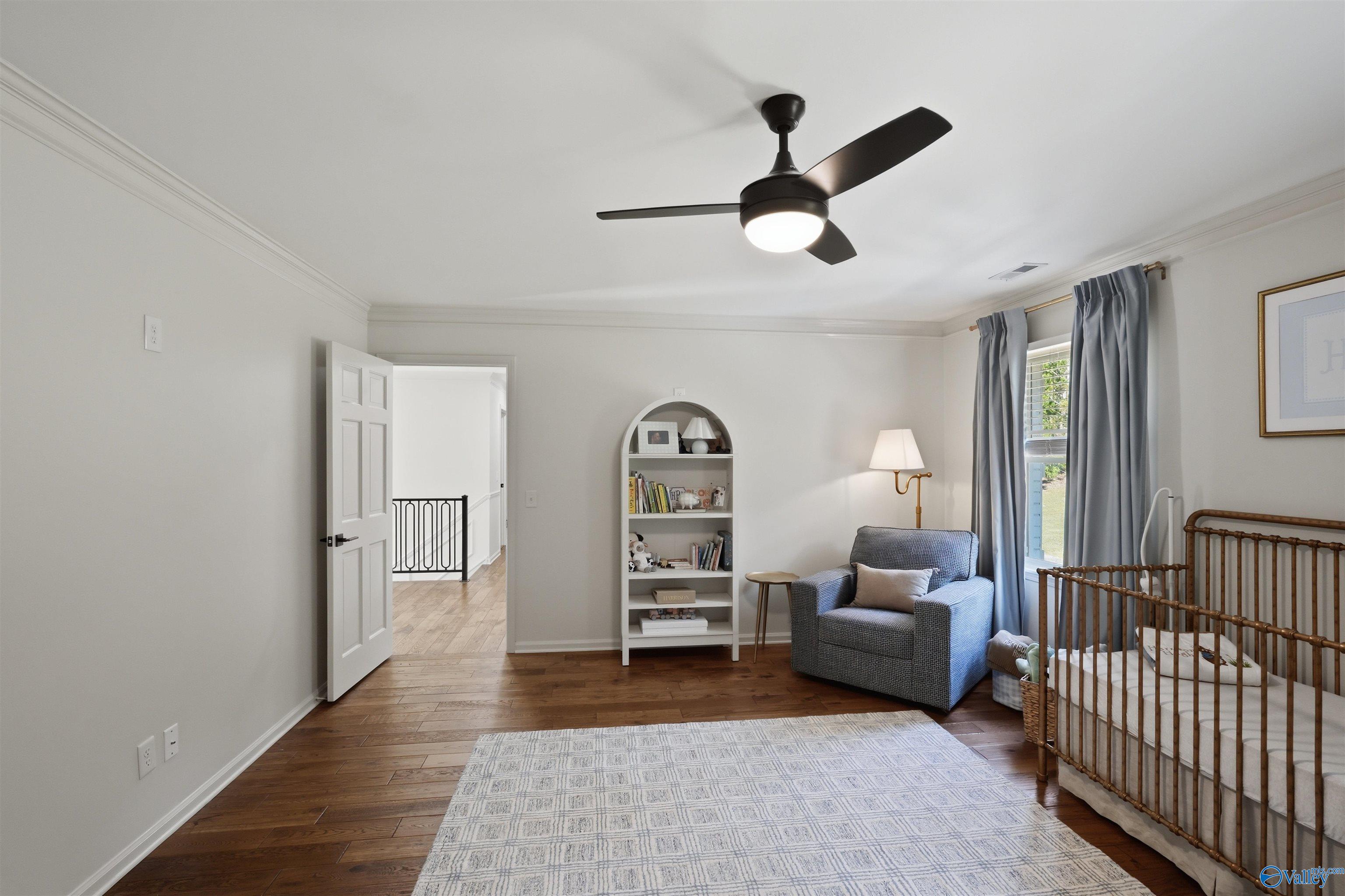 Nursery bedroom with a wooden crib, blue-gray armchair, and white bookcase beside a curtained window.
