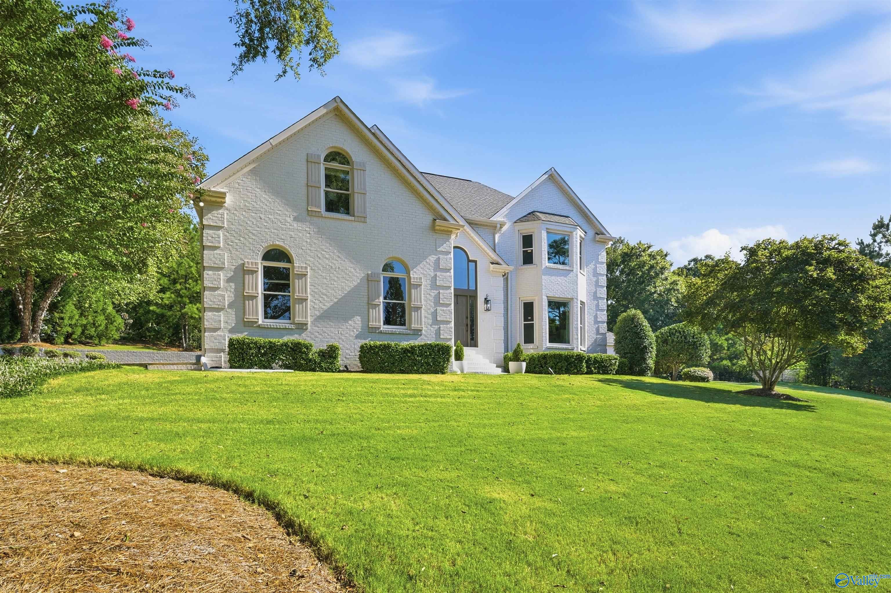 Two-story light-brick house with gabled roof and arched windows beyond a broad green lawn.