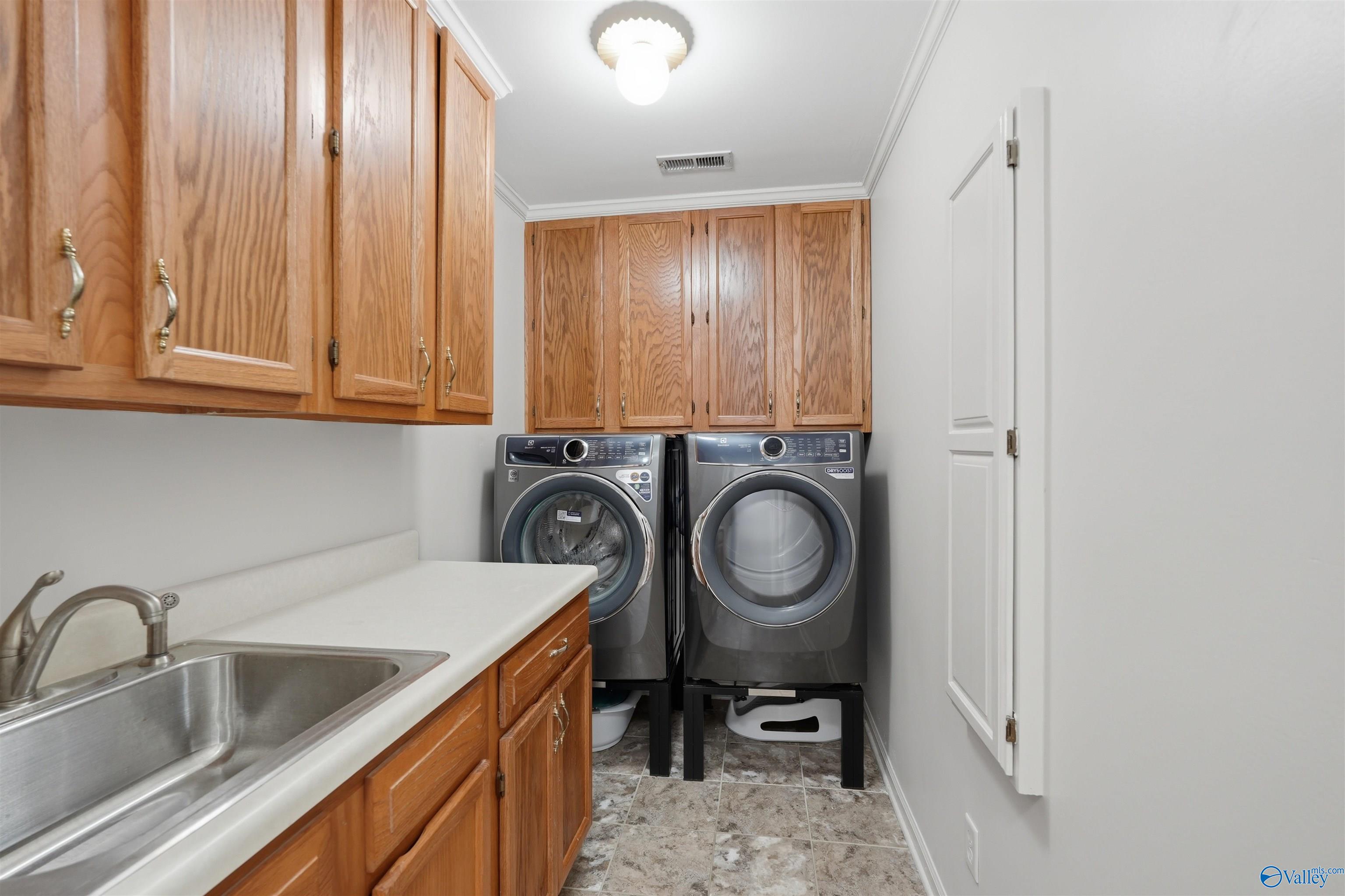 Laundry room with front-loading washer and dryer, oak cabinets, and a utility sink.