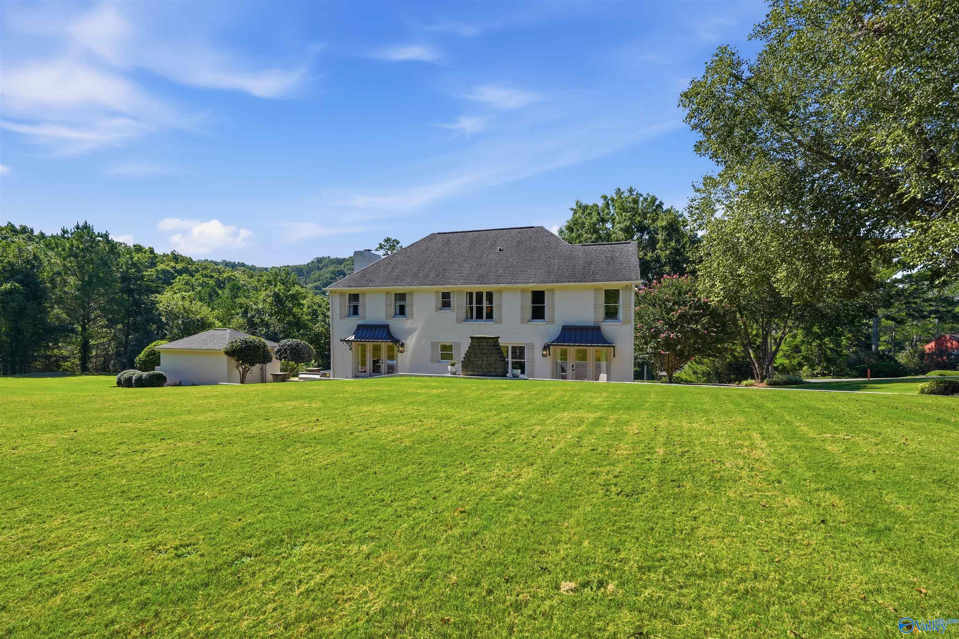 Rear of a white two-story house with blue awnings, a detached outbuilding, and a broad lawn.
