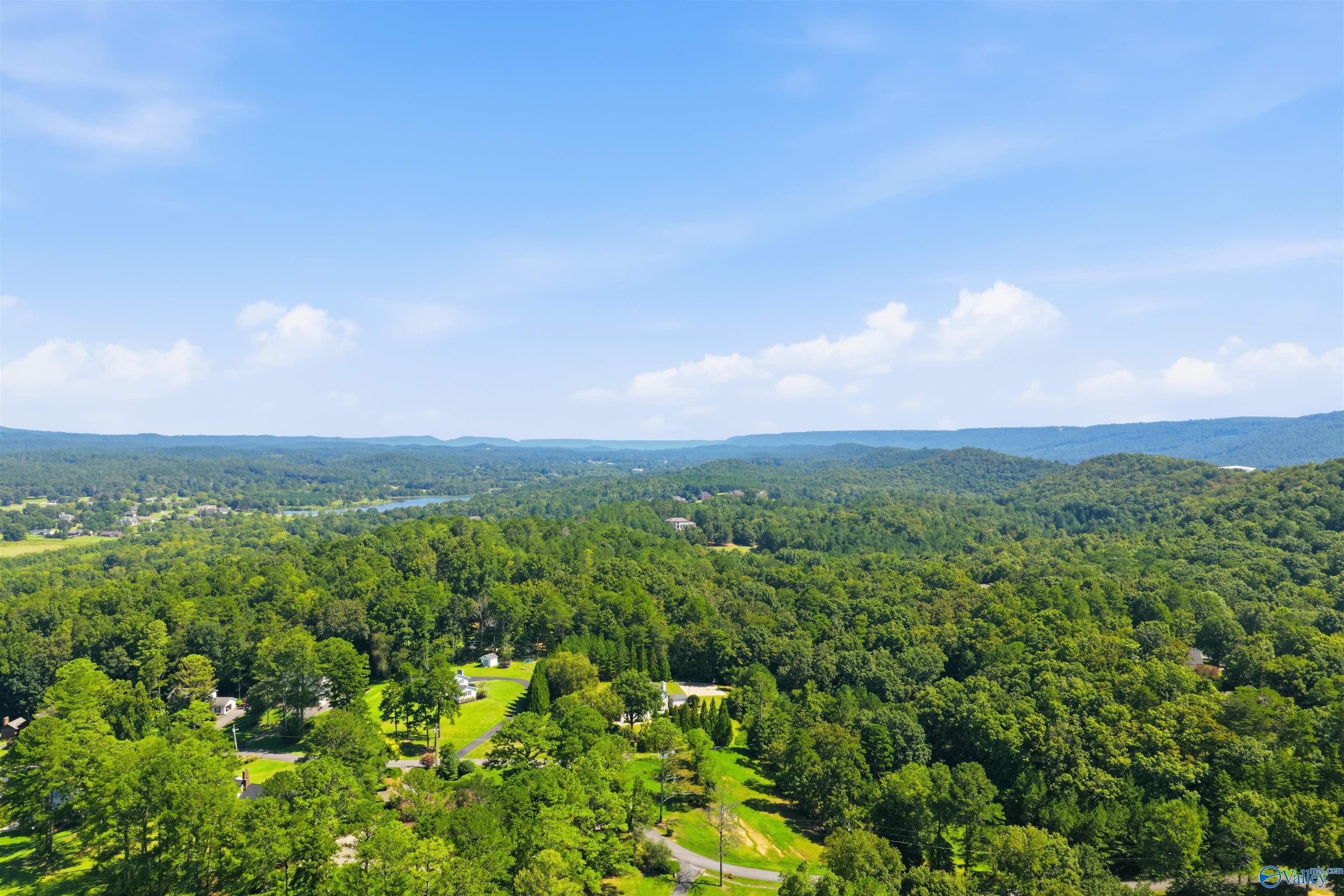 Aerial view of a wooded valley with scattered homes, a small lake, and distant ridges.