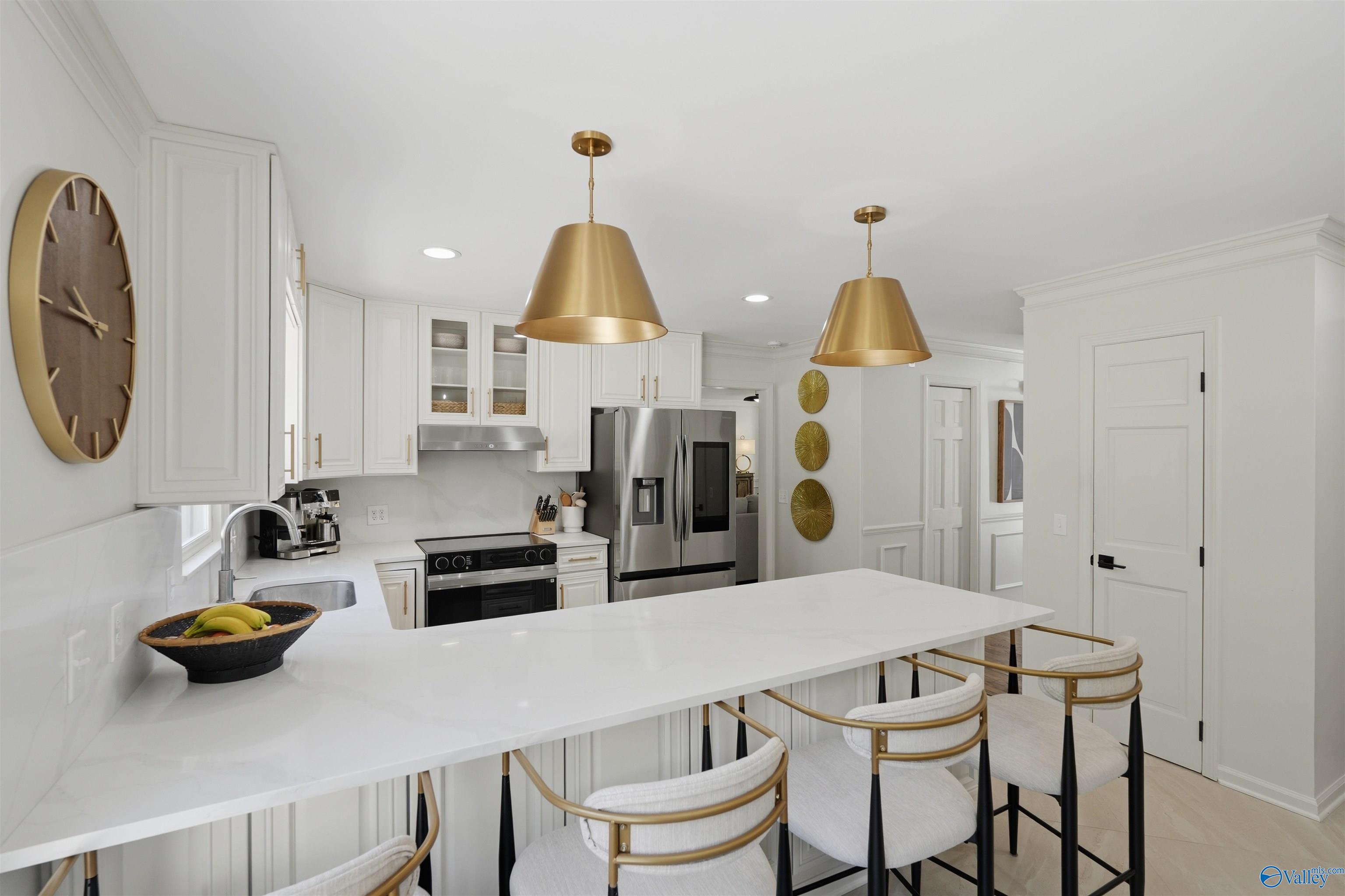White kitchen with a large island, brass pendant lights, and stainless steel appliances.