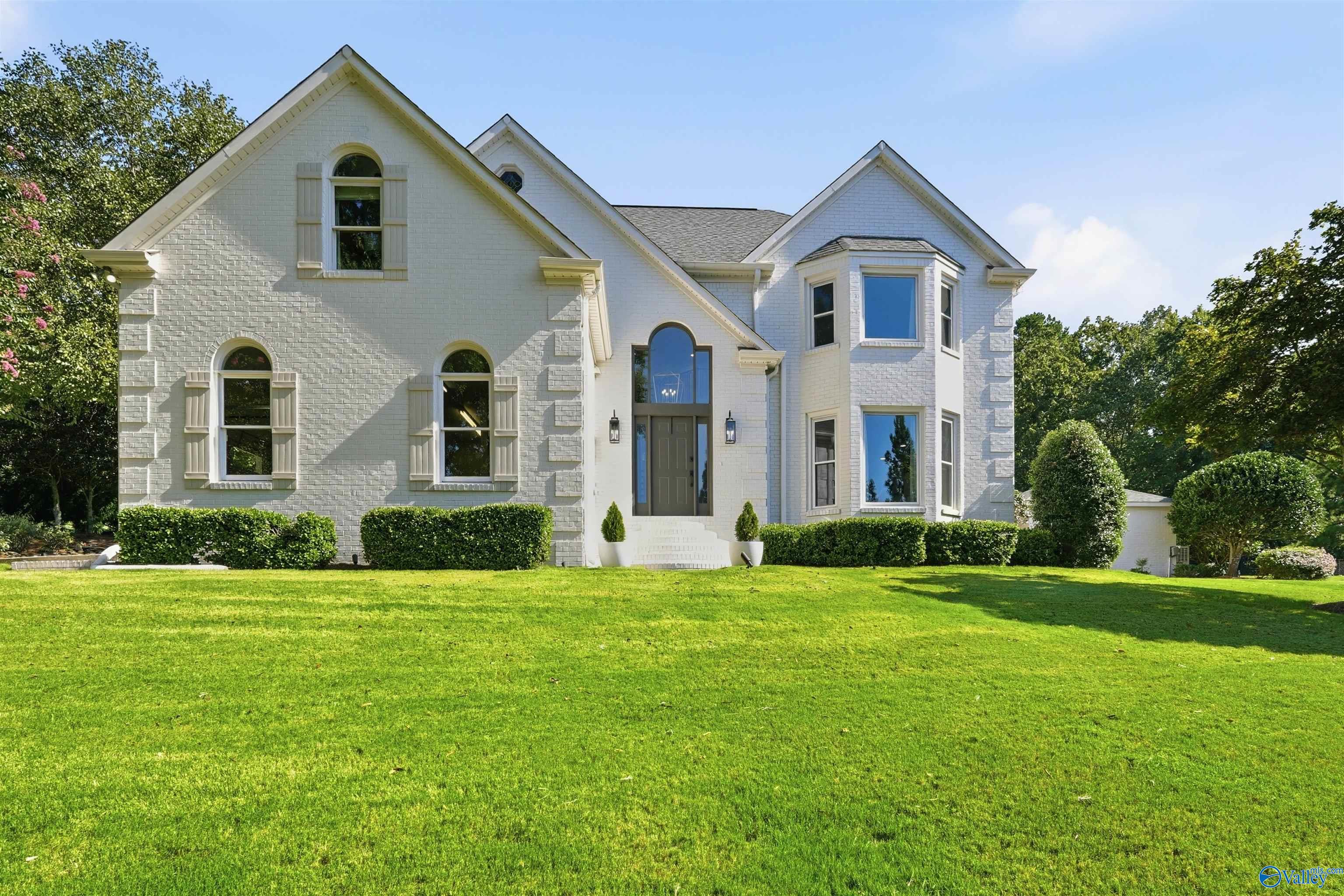 White brick house with multiple gables, arched windows, and a broad green lawn.