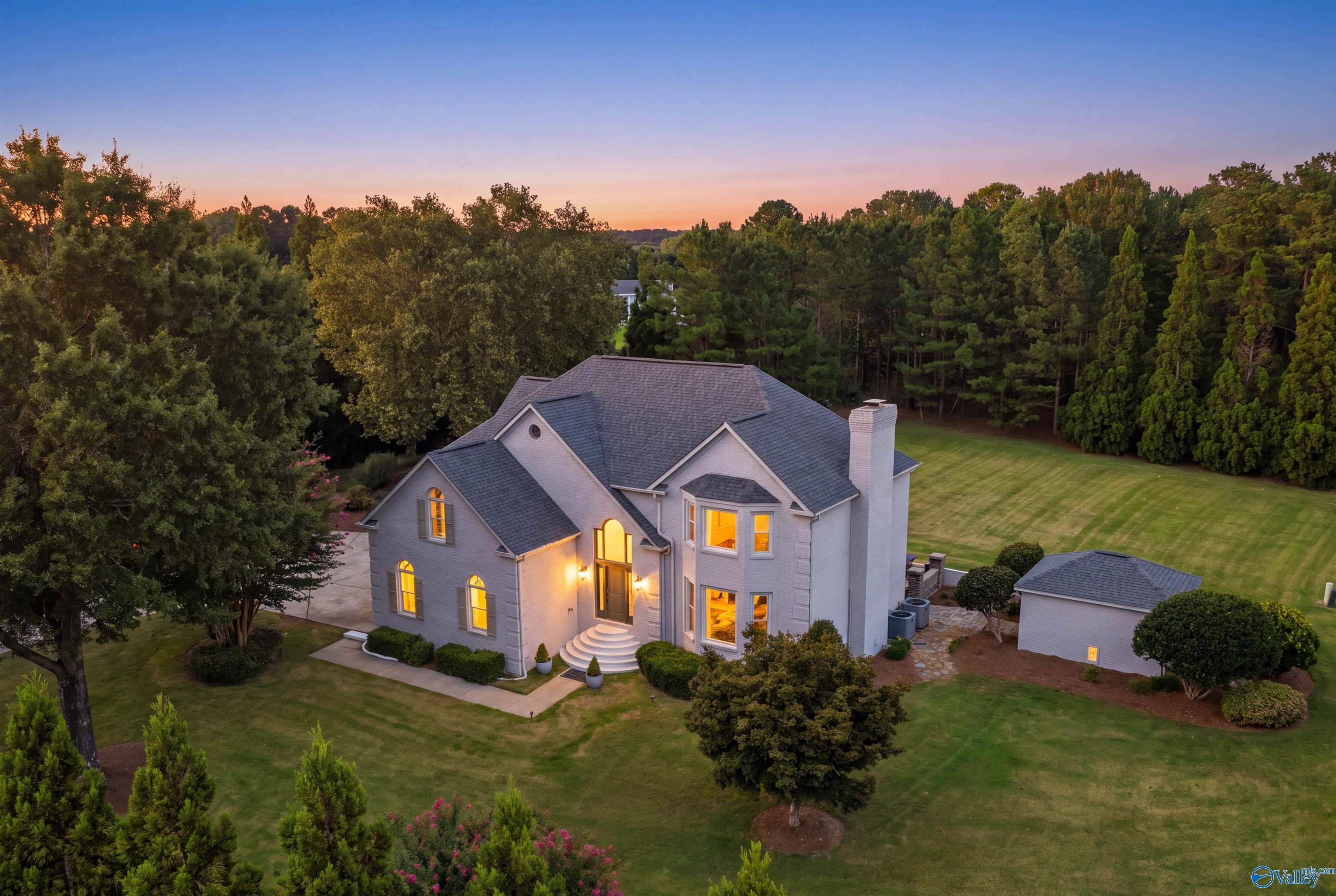 Aerial view of a large gray home with a lit arched entry and detached outbuilding at dusk.