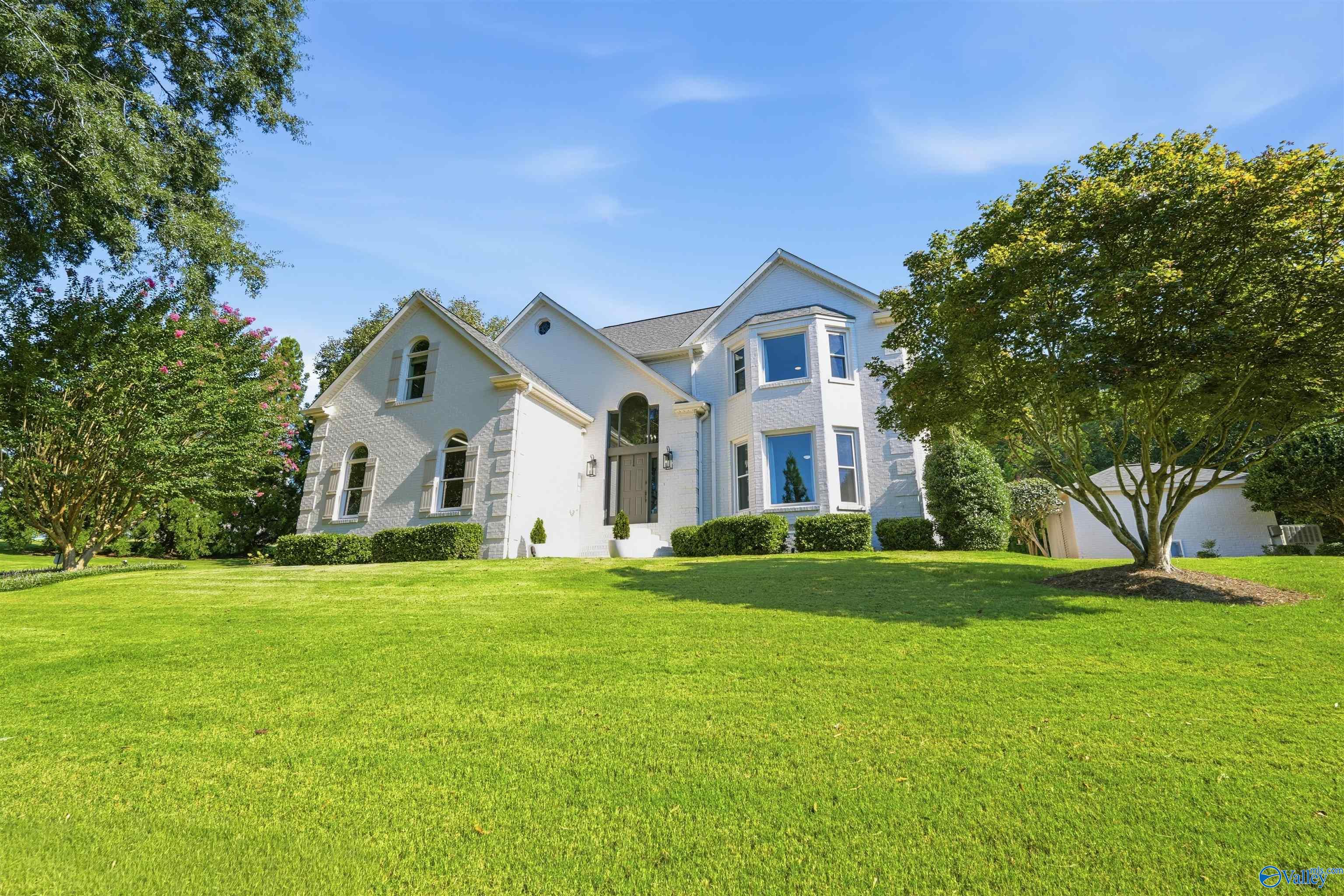 White brick two-story home with arched windows, a bay window, and a broad green lawn.