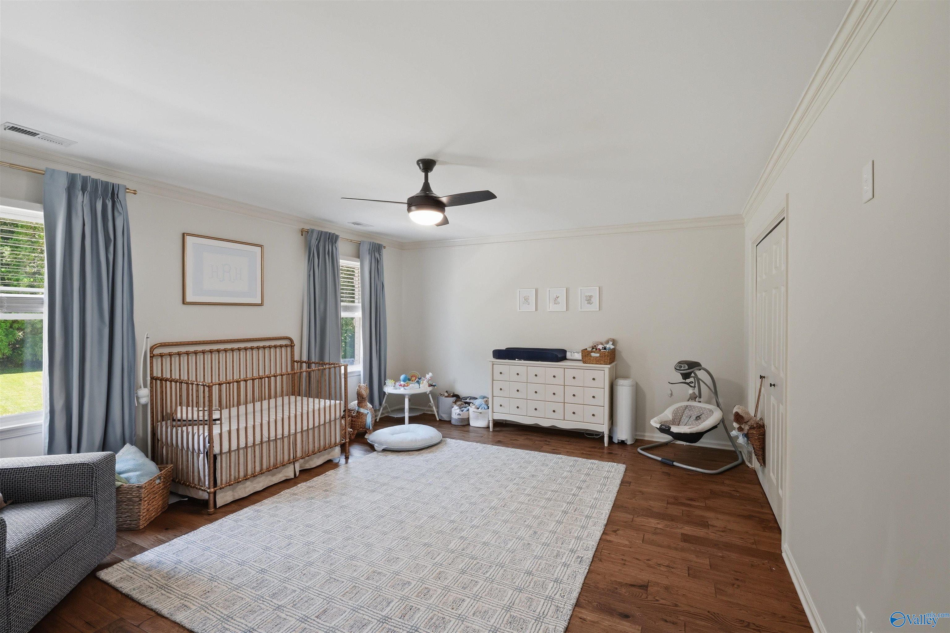 Nursery with a wooden crib, white dresser, baby rocker, and large patterned rug.