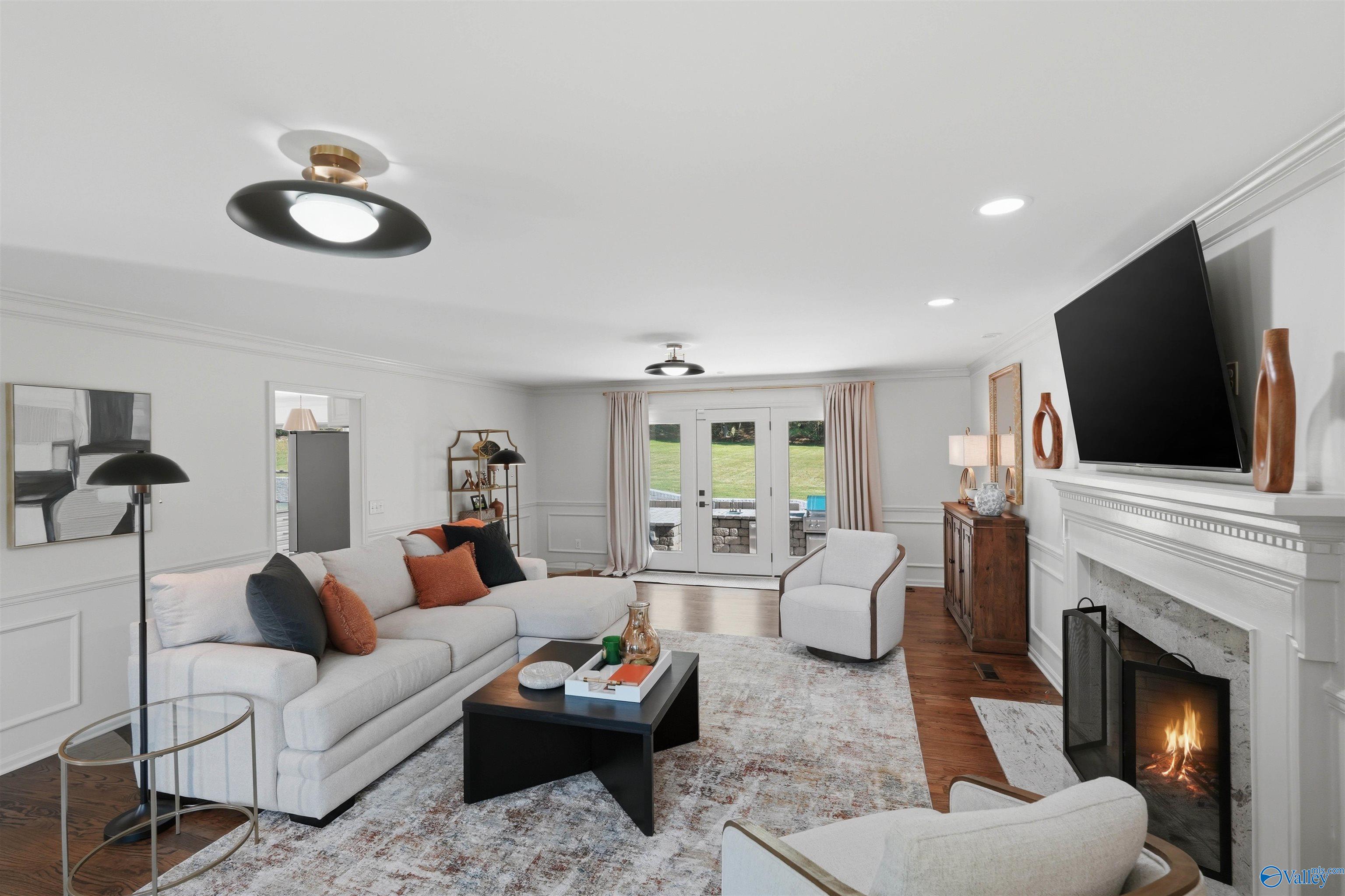 Living room with a lit fireplace, white seating, and glass doors opening to a patio.