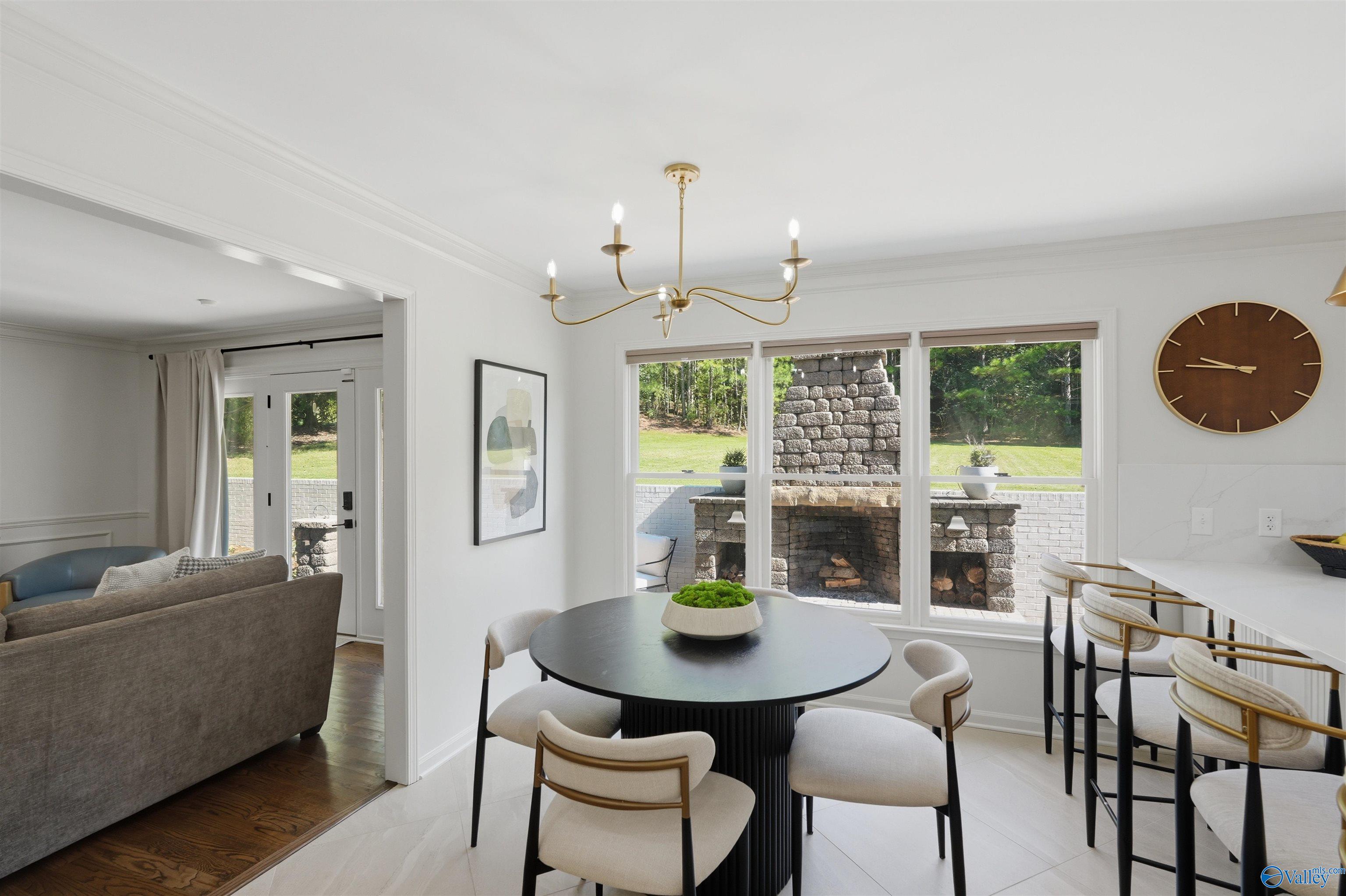 Dining area with a round black table, large windows, and a view of an outdoor stone fireplace.