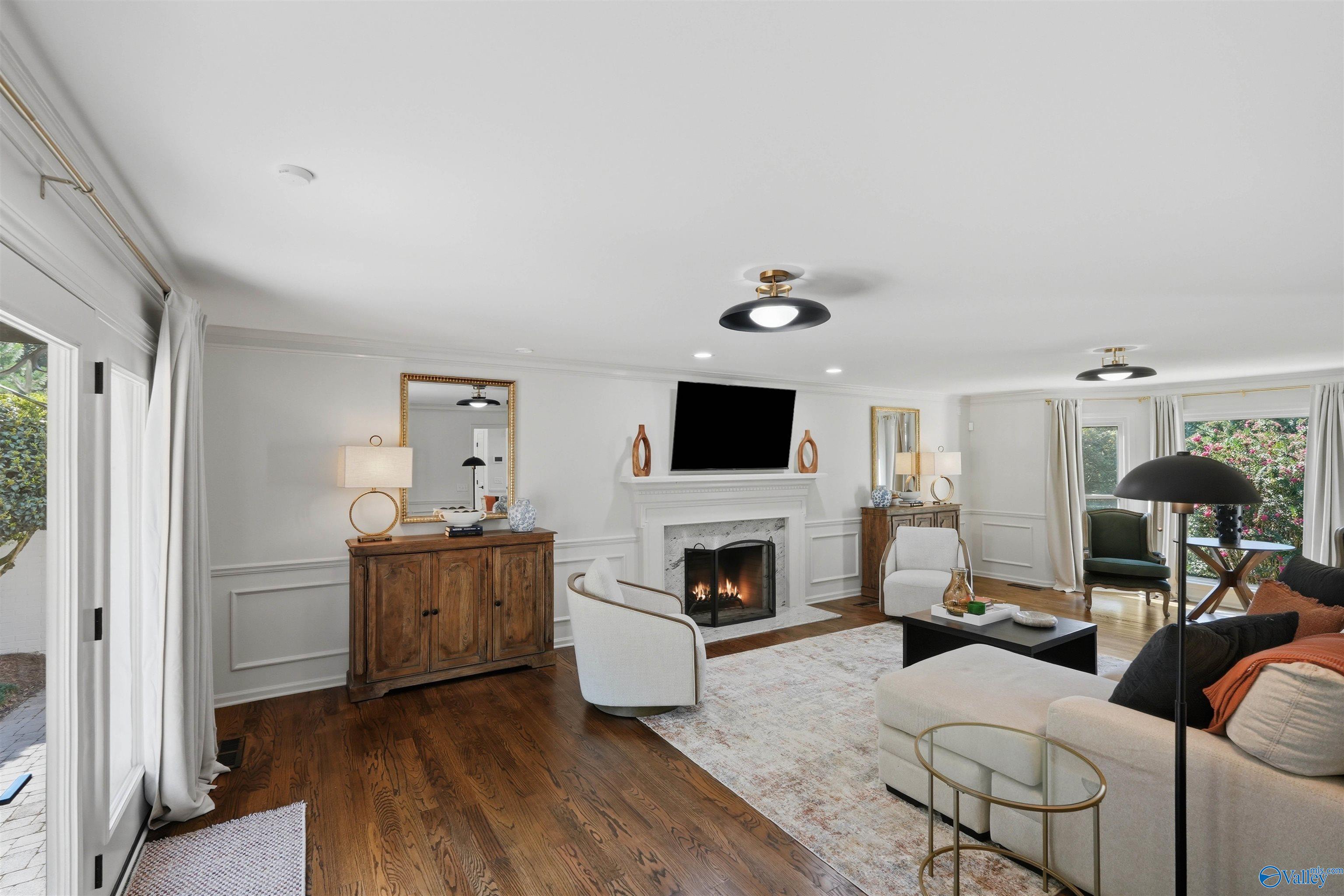 Living room with a white fireplace, mounted TV, hardwood floors, and large windows.