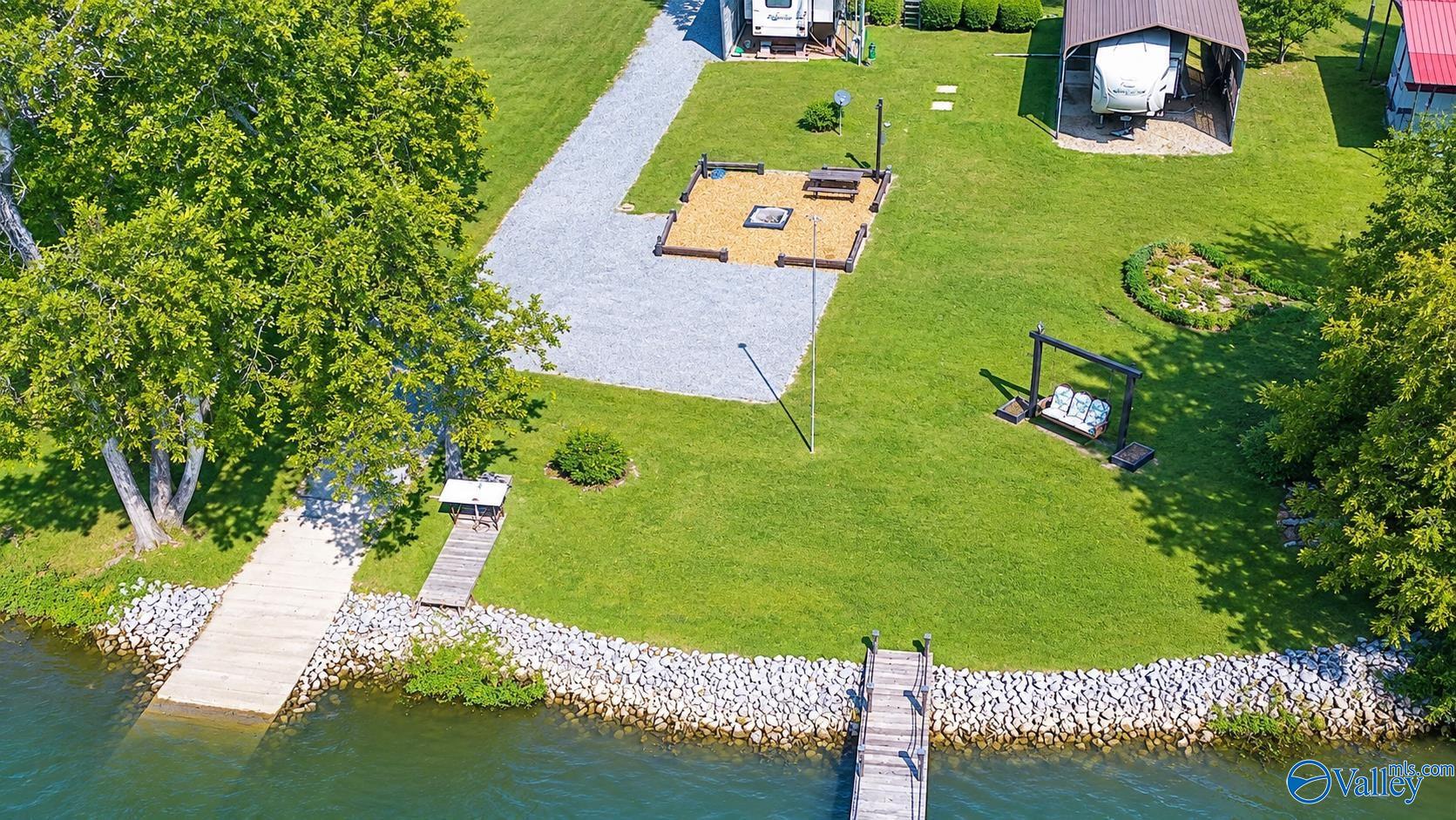 Waterfront property with two docks, a landscaped lawn, fire pit, and covered RV parking.
