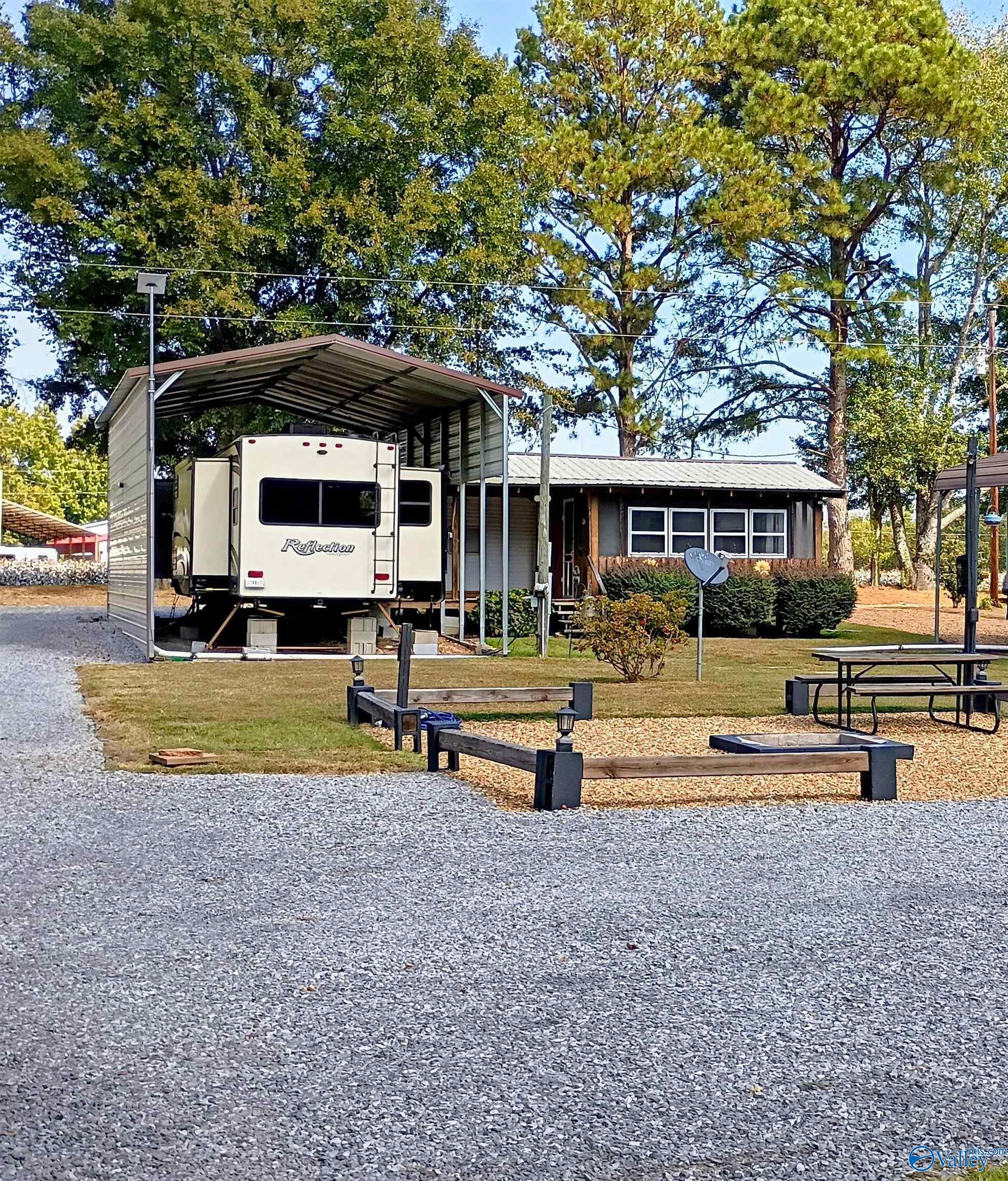 Single-story home beside an RV under a metal carport, with a gravel drive and picnic area.