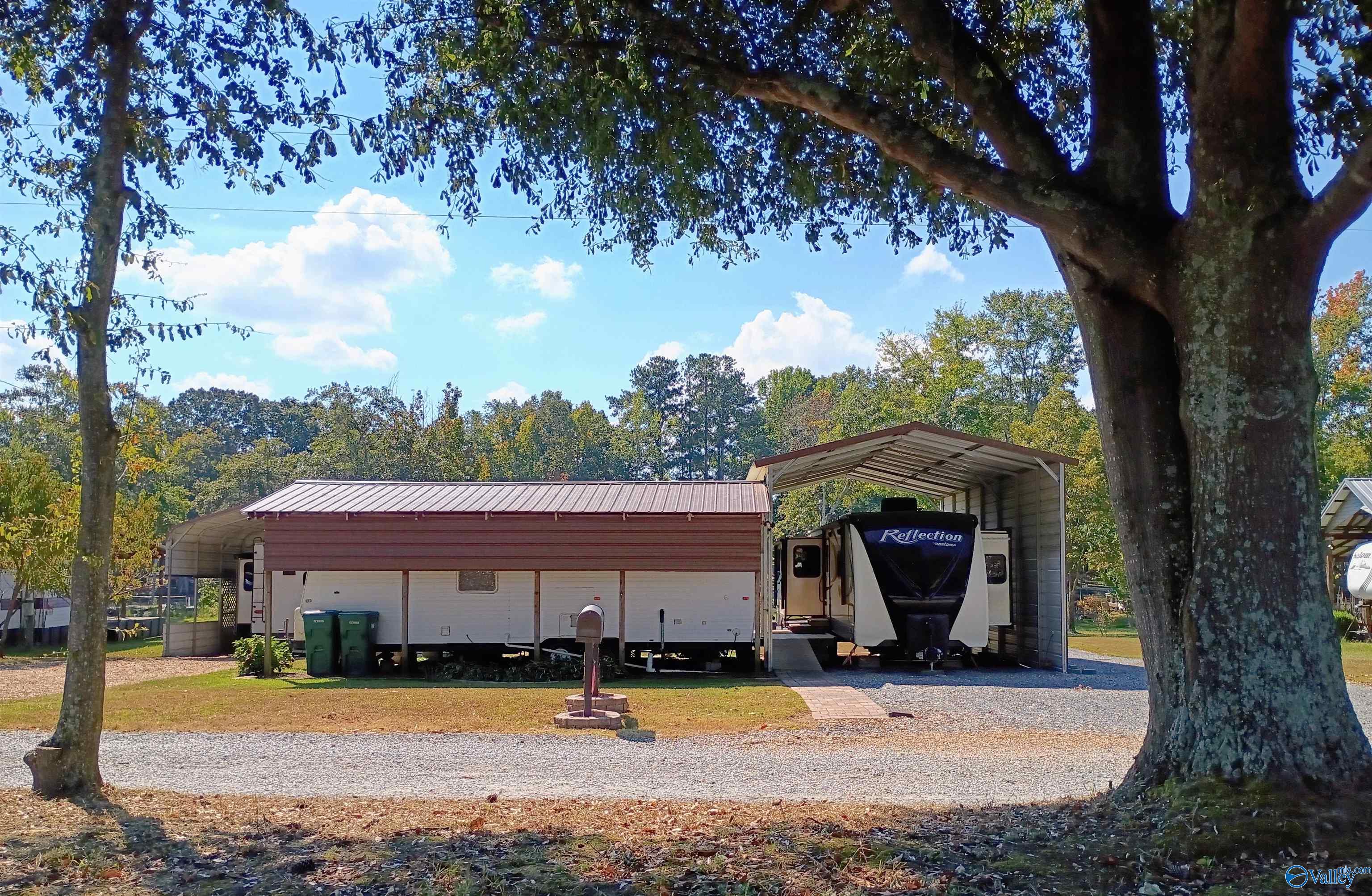 RV shelters and parked recreational vehicles beneath mature trees, with a gravel drive and mailbox.