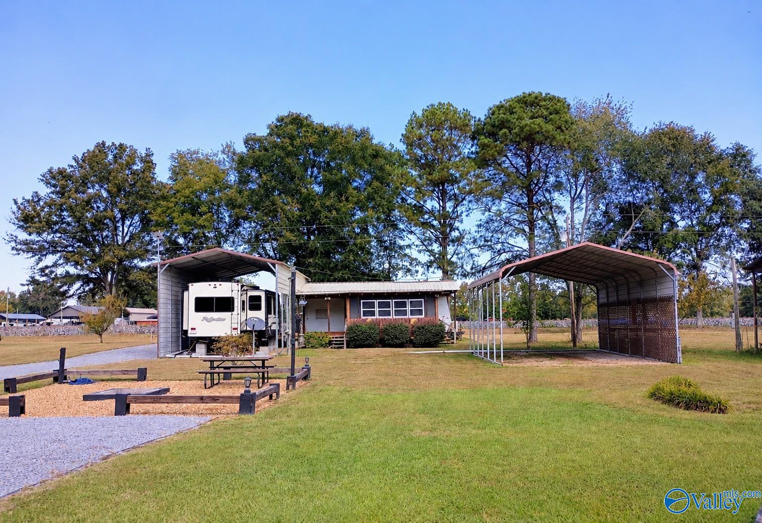 Small single-story home with an RV under a shelter and a second metal-roofed shelter nearby.
