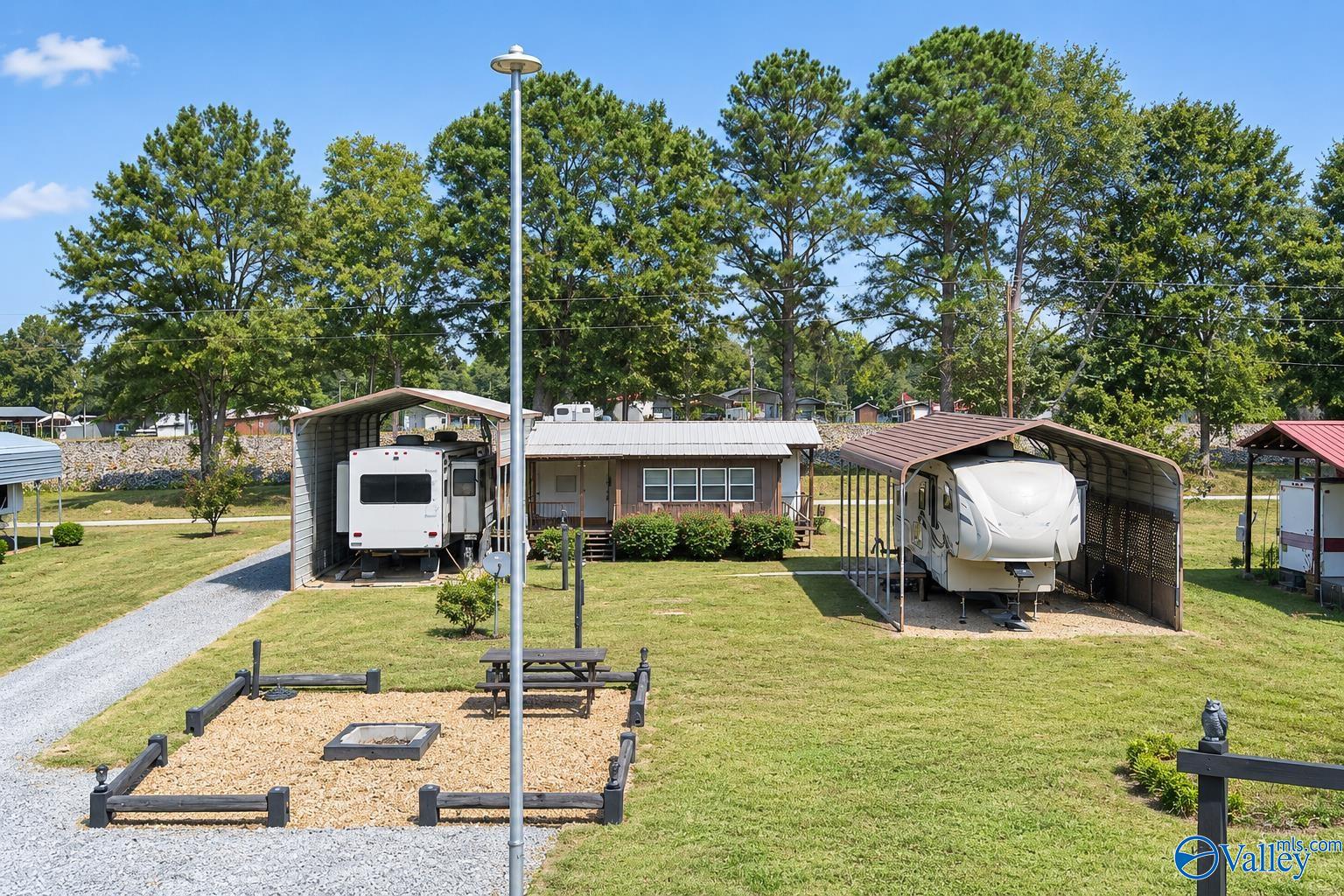 RV property with a small cabin, two covered RVs, gravel drives, and a fire pit area.