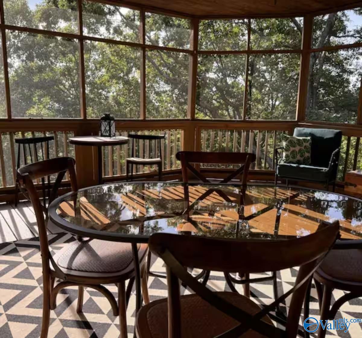 Screened porch dining area with a glass-top table, wooden chairs, and leafy tree views.