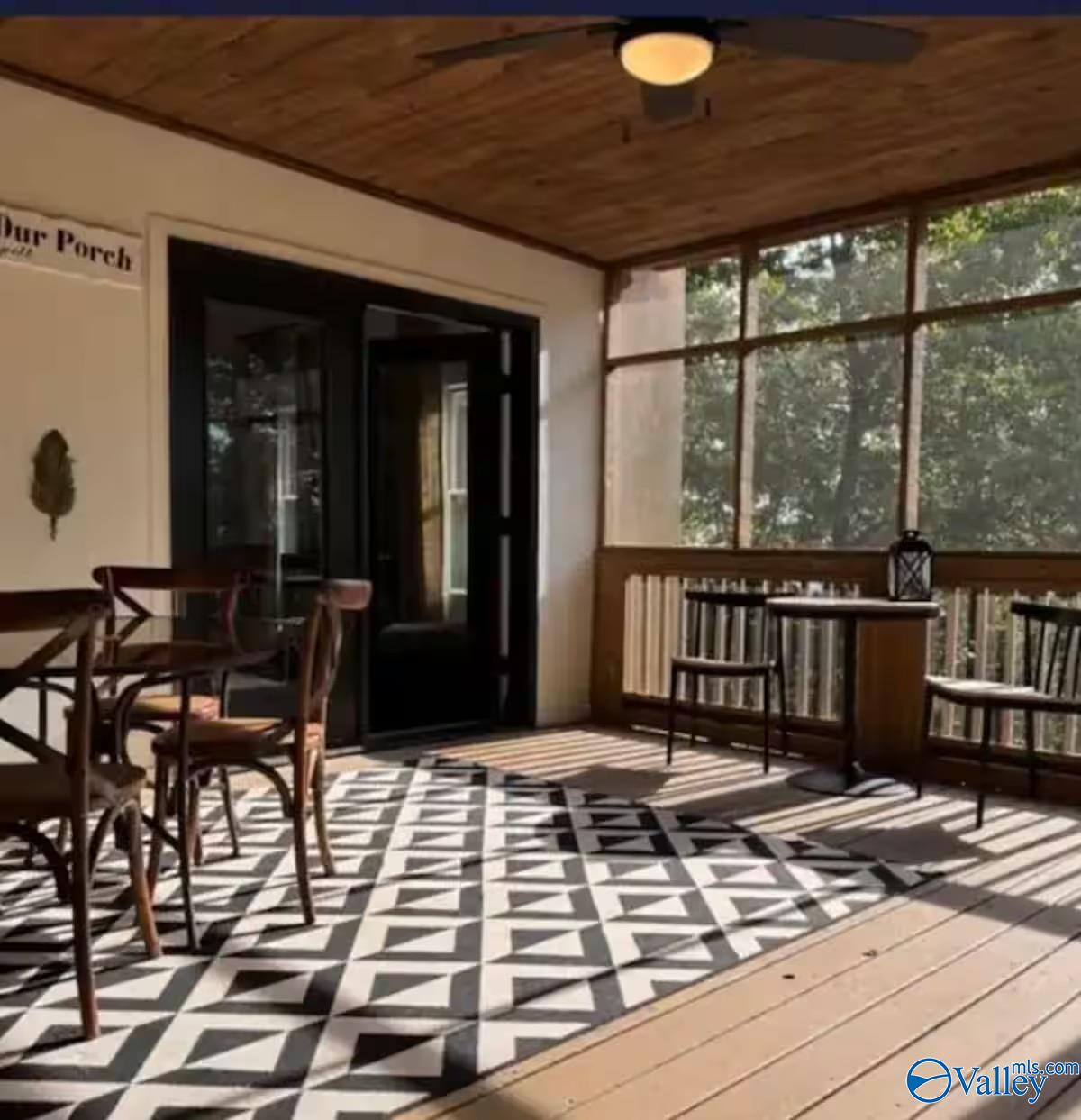 Screened porch with a wood ceiling, geometric rug, dining chairs, and wooded views.