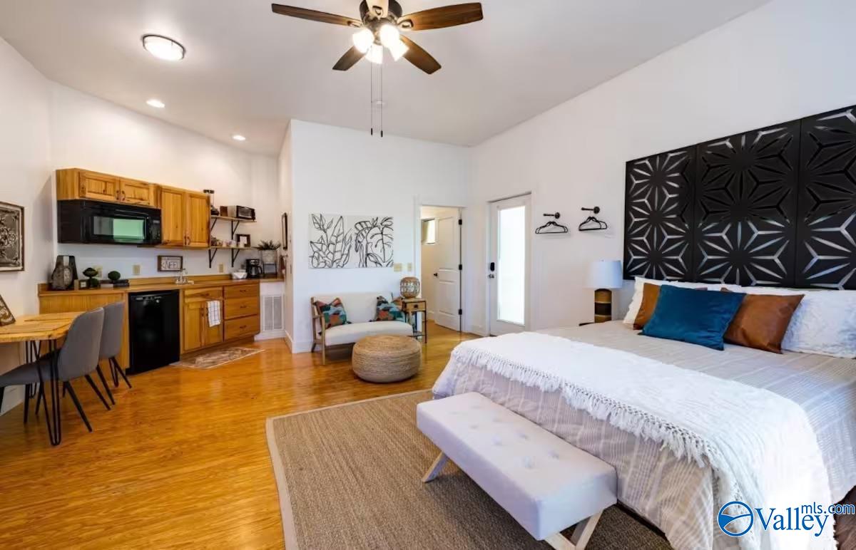 Furnished bedroom with kitchenette, hardwood floors, and a bold black geometric headboard.
