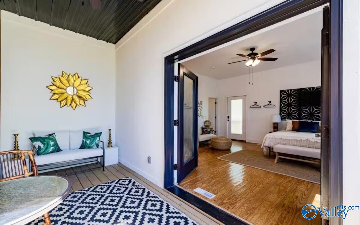 Furnished covered porch with a white sofa opens into a bedroom with hardwood floors.