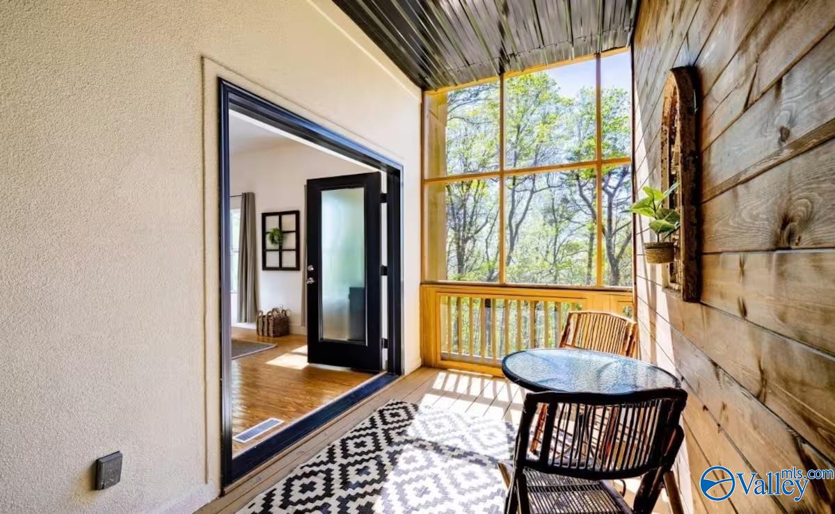 Furnished covered porch with a round table, patterned rug, and large windows overlooking trees.