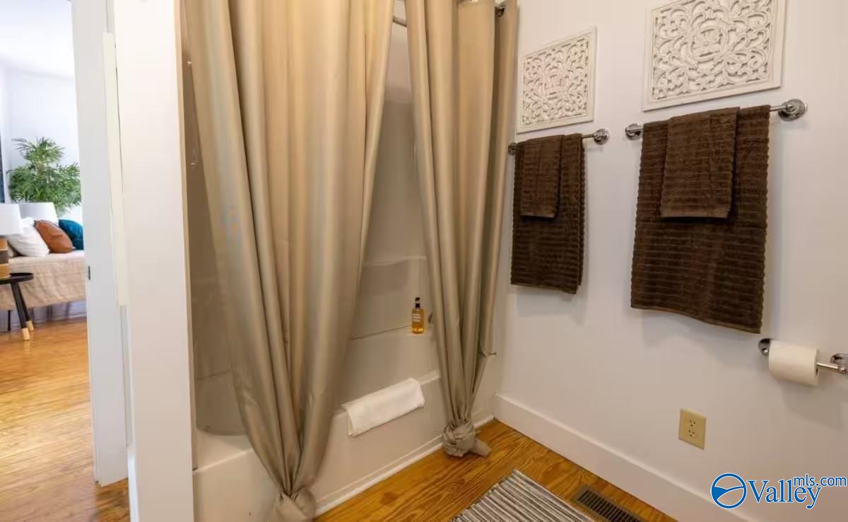 Bathroom with a curtained tub-shower, dark towels, and hardwood flooring.