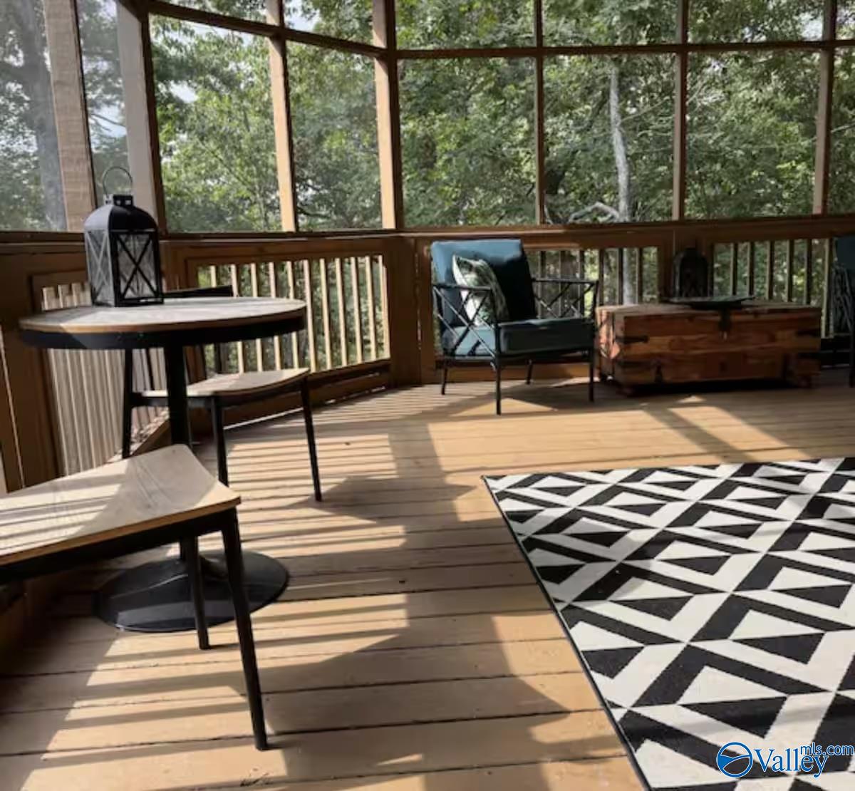 Screened-in porch with wood floors, seating, and a view of leafy trees.
