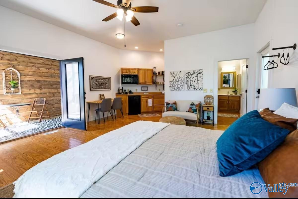 Bedroom with a bed, open kitchenette, rustic wood accent wall, and open patio door.