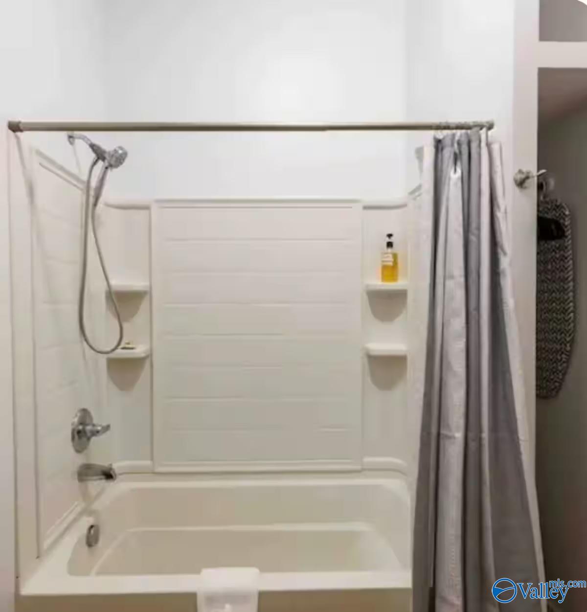 Bathroom with a white tub-shower combo, built-in corner shelves, and a gray curtain.