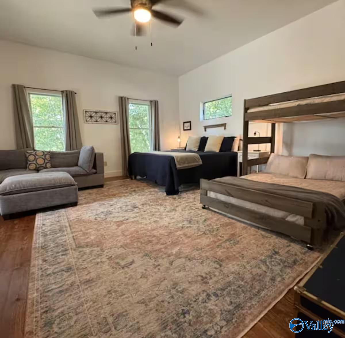 Furnished bedroom with a wooden bunk bed, a second bed, and a gray sofa.
