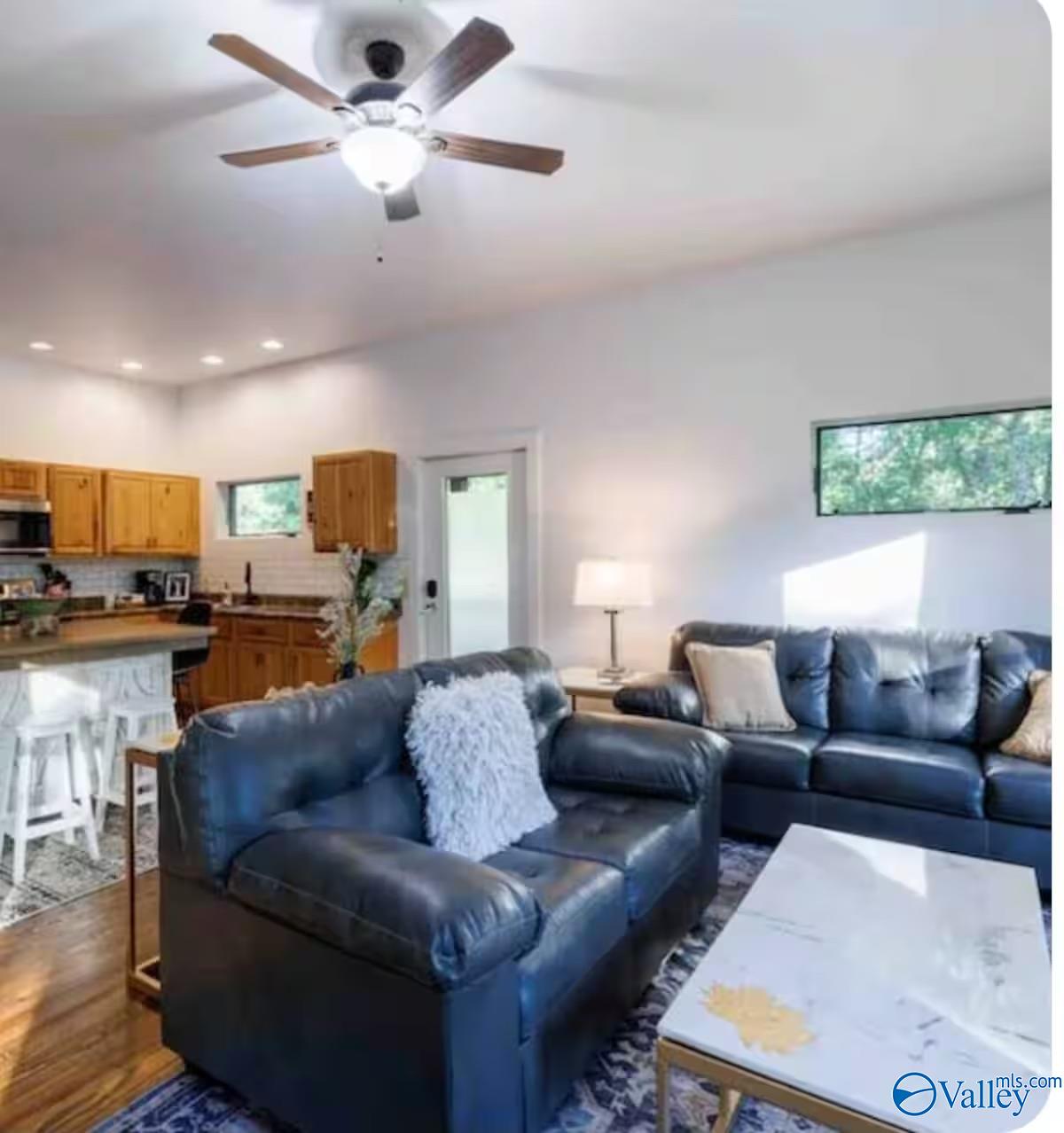 Open-plan living room with blue leather sofas, white coffee table, and adjoining wood-cabinet kitchen.