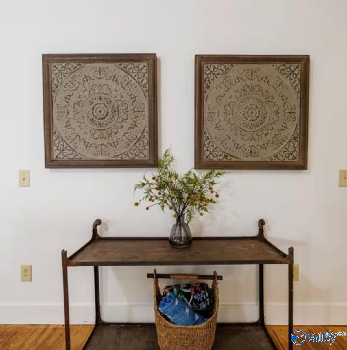Wood console table with a vase of greenery and woven basket beneath two framed artworks.