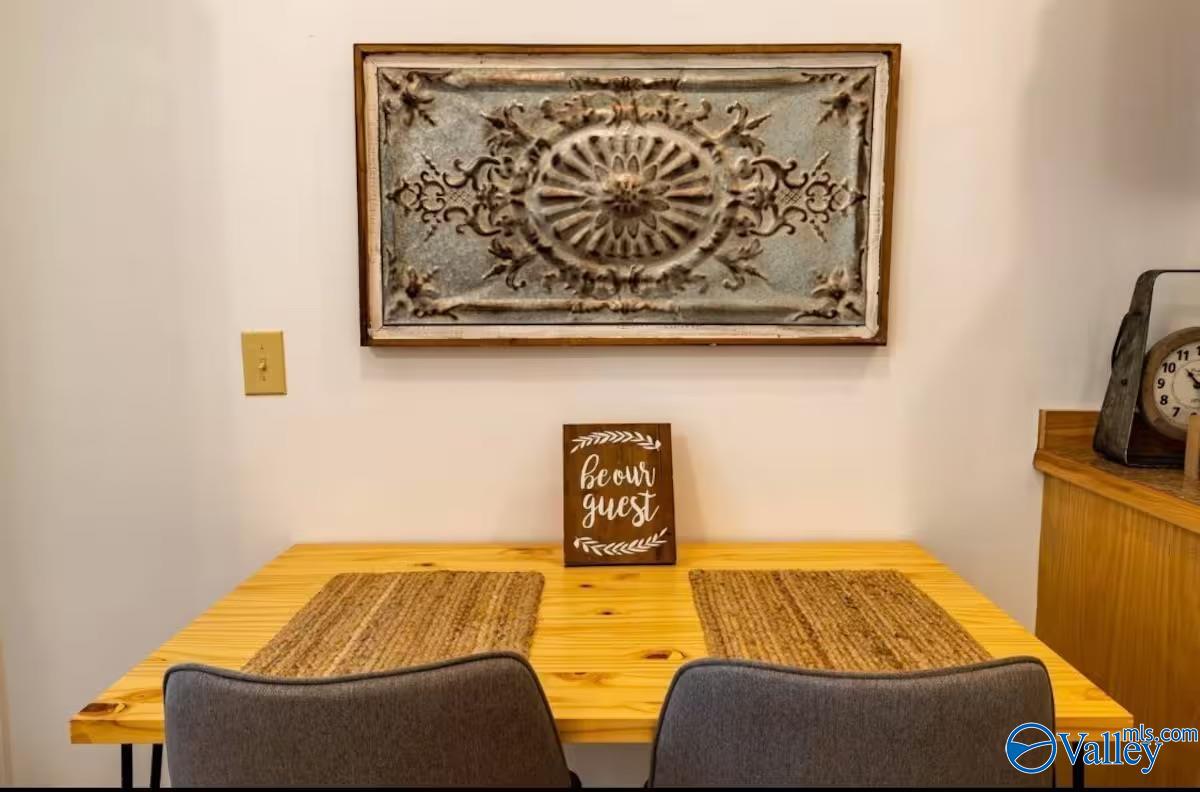 Dining area with a wooden table, woven placemats, and framed wall art above a “be our guest” sign.