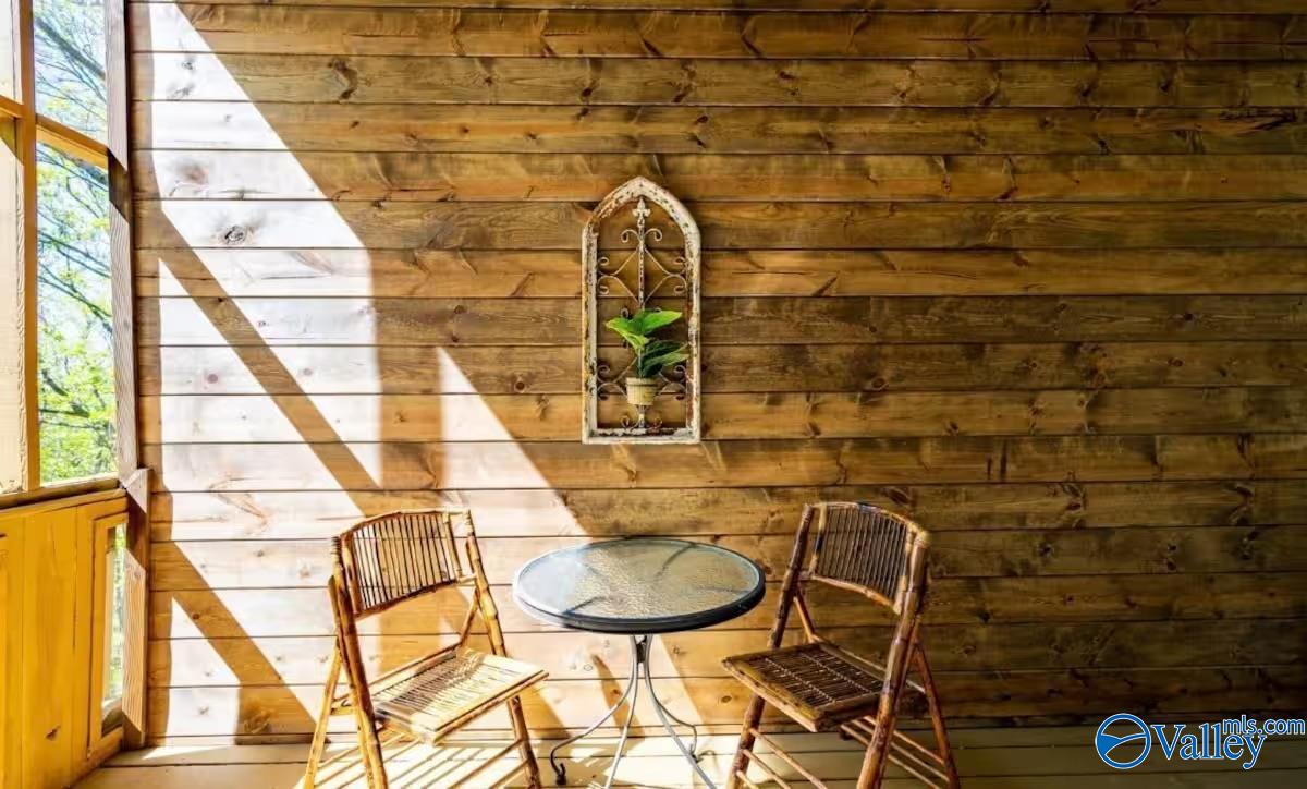 Enclosed wood-paneled porch with tall windows, two folding chairs, and a round glass-top table.