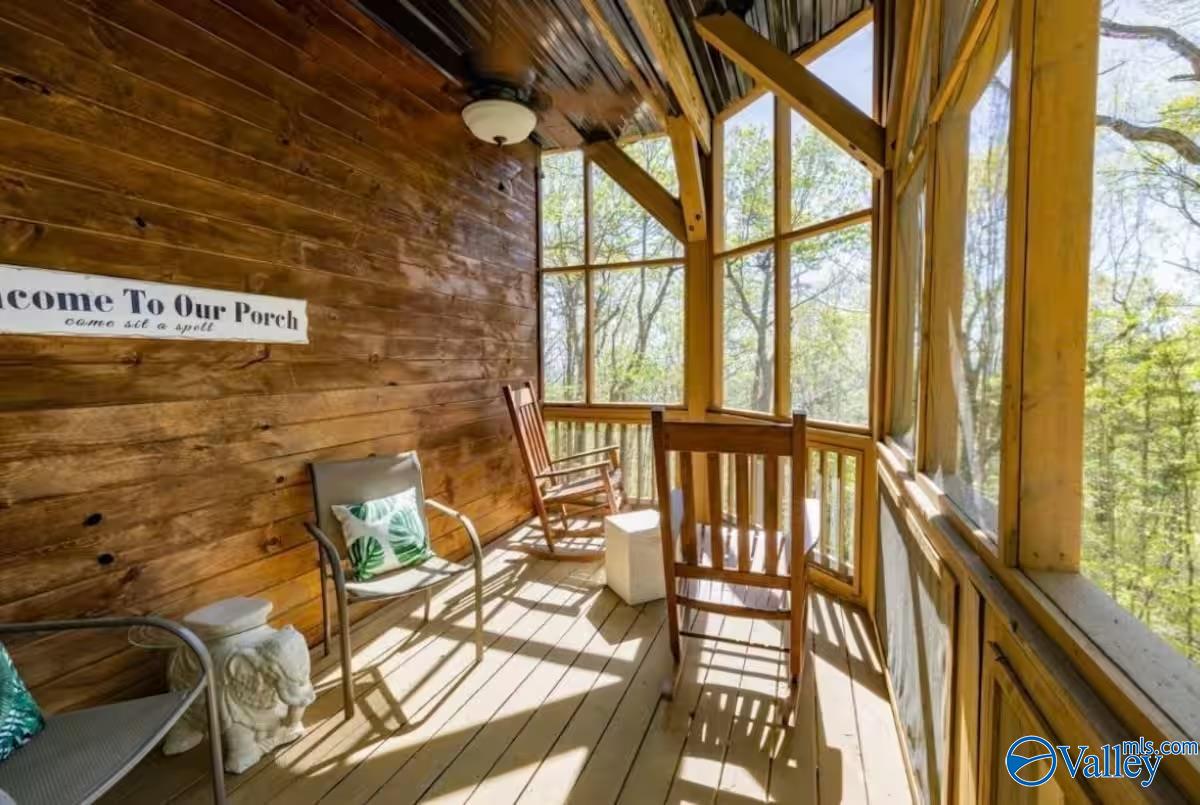 Screened porch with wood walls, tall windows overlooking trees, and rocking chairs.