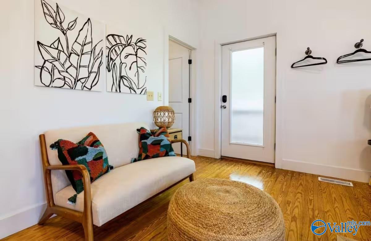 Furnished entryway with a cream settee, woven ottoman, hardwood floors, and botanical wall art.