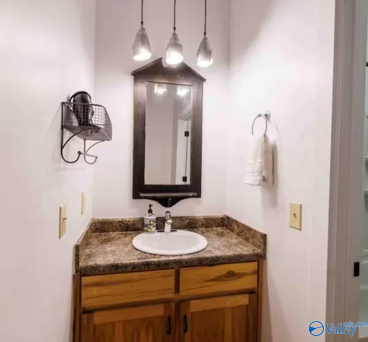 Bathroom vanity with a brown stone countertop, wood cabinets, dark-framed mirror, and three pendant lights.