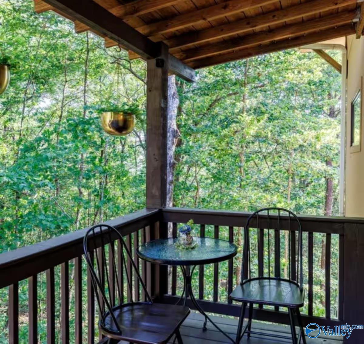 Covered wooden porch with a table and chairs overlooking dense woods.