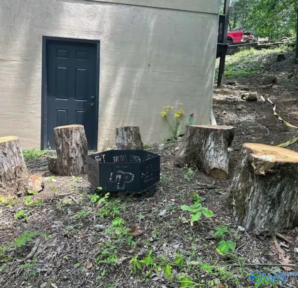 Outdoor fire pit ringed by tree-stump seats beside a small outbuilding.